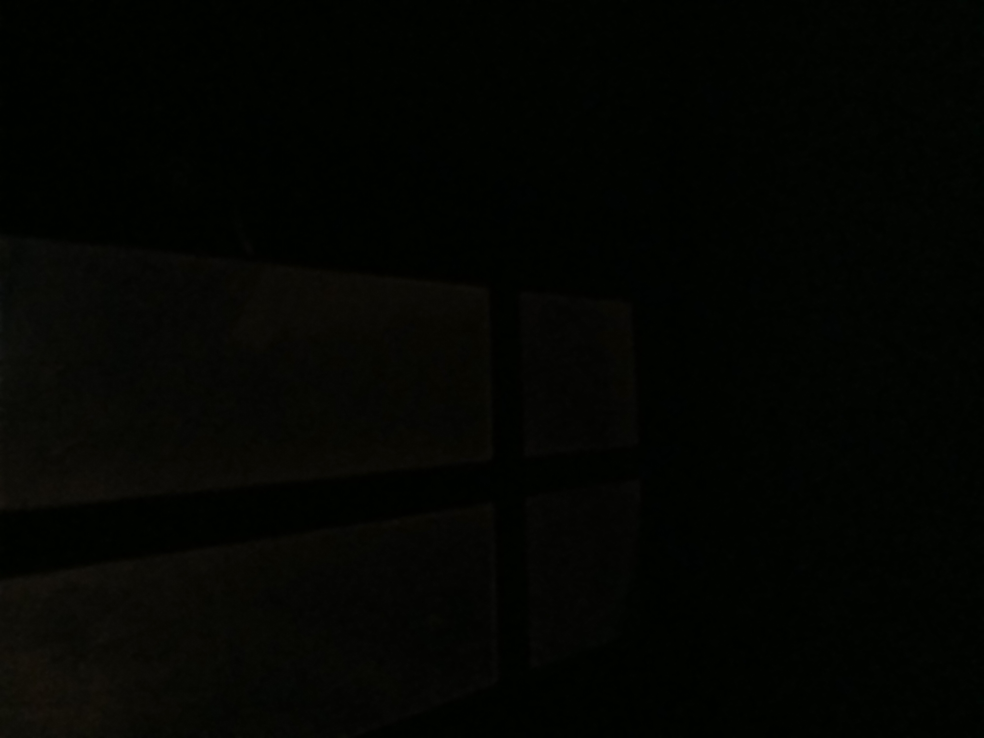 The image depicts a dark, abstract scene with faint geometric patterns suggesting a window or grid structure in the upper left quadrant. The majority of the image is black, obscuring any discernible objects or details. Due to the lack of visual information, it is impossible to determine the specific location, including its presence in Tenggarang, Indonesia, or to provide any forensic details regarding people, subjects, objects, actions, interactions, or the environment.