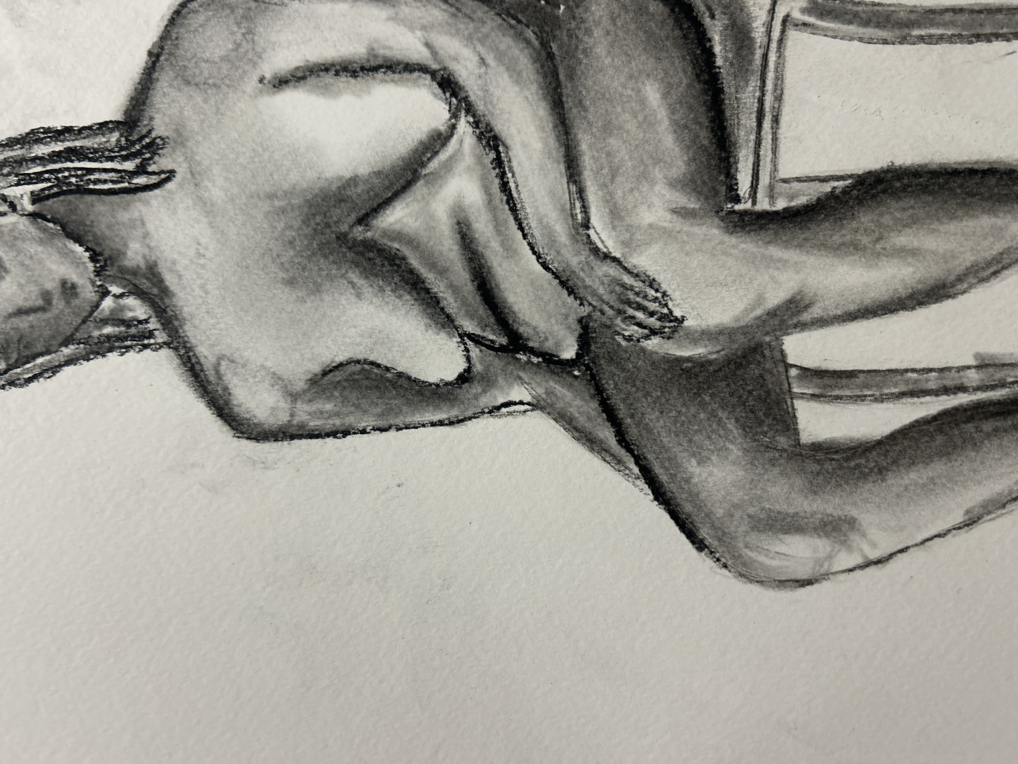 The image is a charcoal drawing of a nude figure seated on a chair. The figure is rendered in shades of gray with dark outlines defining the body and chair. The figure's legs are intertwined, and their hand rests upon their leg. The chair is simple with a horizontal back. The background is plain white paper. There is no information in the image to definitively place the location in Sofia, Bulgaria or any other place.