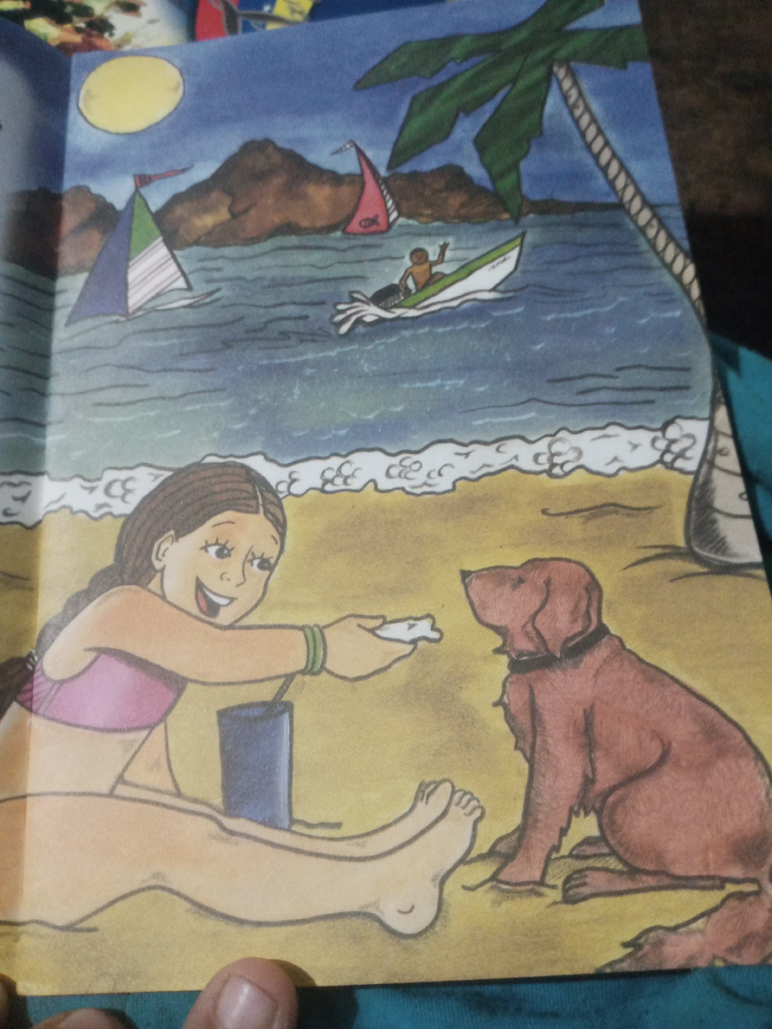 A girl with brown braided hair, wearing a pink swimsuit, sits on a sandy beach offering a small white object to a brown dog. The dog, wearing a black collar, sits attentively in front of her. In the background, blue ocean waves gently lap the shore, with several sailboats visible on the water. Mountains rise in the distance under a yellow sun. A palm tree with green fronds leans over the scene. The image depicts a sunny day at the beach in Santa Ana, Venezuela.