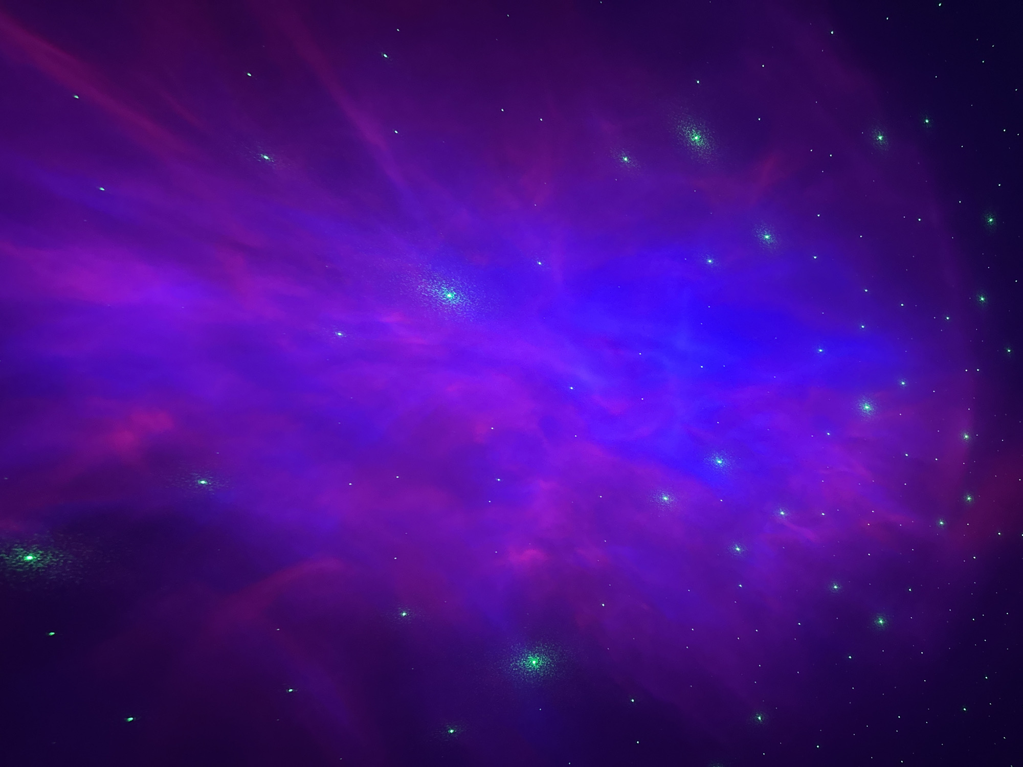 A digital illustration depicts a nebula with a color palette of purple, blue, and green. The background primarily consists of a purple haze, overlaid with streaks of pink and deep blue, creating a textured, cloud-like effect. Scattered throughout are numerous small, green dots that resemble stars. The image does not contain any recognizable city elements or indications of location. There are no people, subjects, objects, actions, or interactions depicted. The environment is strictly astronomical.