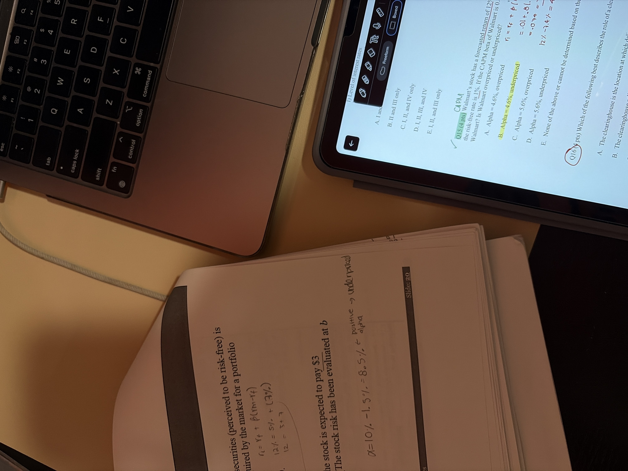 A close-up image shows a workspace with a laptop, an iPad, and a stack of papers. The laptop, likely a MacBook, has its keyboard visible. The iPad displays digital notes on what appears to be finance or investment analysis, with a question about Walmart being overpriced or underpriced marked as correct. Below the iPad, a paper contains handwritten notes and calculations related to stock valuation and risk assessment. The notation mentions an "alpha," denoting positive or negative returns and whether a stock is underpriced or overpriced. The environment is a light-colored surface, possibly a desk. The details suggest the scene is set in an office or study environment, with a focus on financial analysis and education.