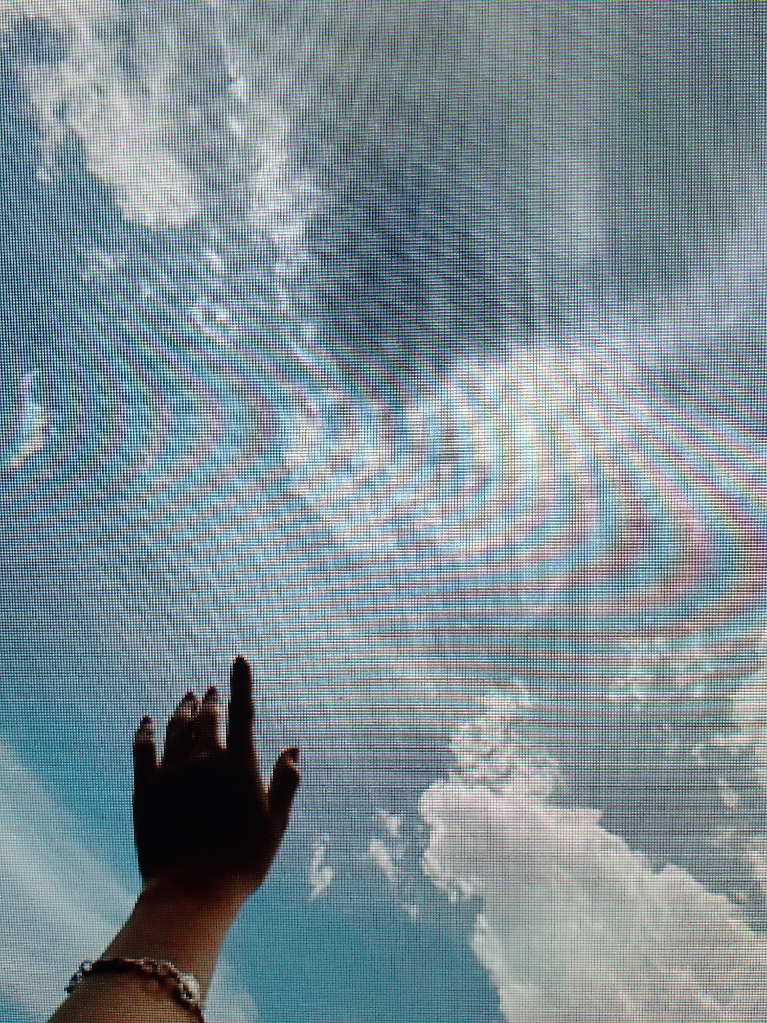 A hand reaches up towards a sky with clouds. The image appears to be captured from a screen. The location is unknown.