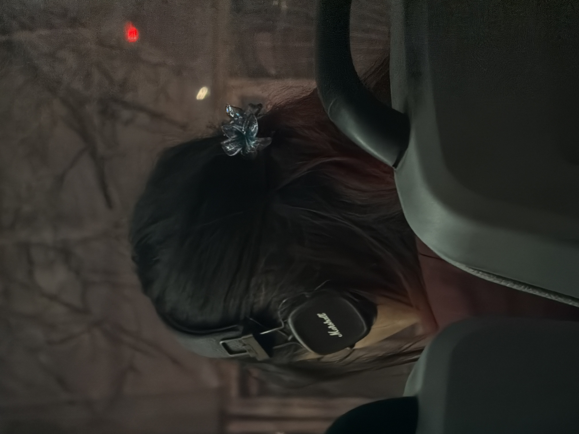 A person with dark hair and a flower-shaped hair clip is wearing Marshall headphones in what appears to be a vehicle. Reflected in the window are blurred images suggesting an urban environment at night, with indications of trees and streetlights. Given the focus on the person, the exact location within Rostov-on-Don, Russia cannot be determined from this image alone.