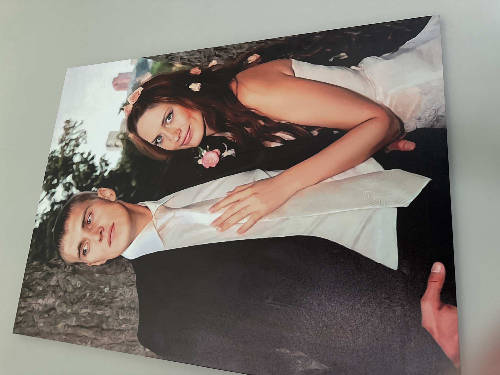 This is a painting of a newlywed couple posed for a portrait. The man is on the left, wearing a black suit jacket and a white dress shirt with a white tie. He is looking to his left, with a serious expression. The woman is on the right, wearing a white wedding dress and a floral hairpiece. She is looking at the viewer with a slight smile. Her hand is resting on the man's chest. The background appears to be a park-like setting with trees and buildings in the distance. The style of the painting is realistic with a soft, painterly quality.
There is no information available in the image or the crops to suggest that the location is the city of Konstantinovo, Russia.