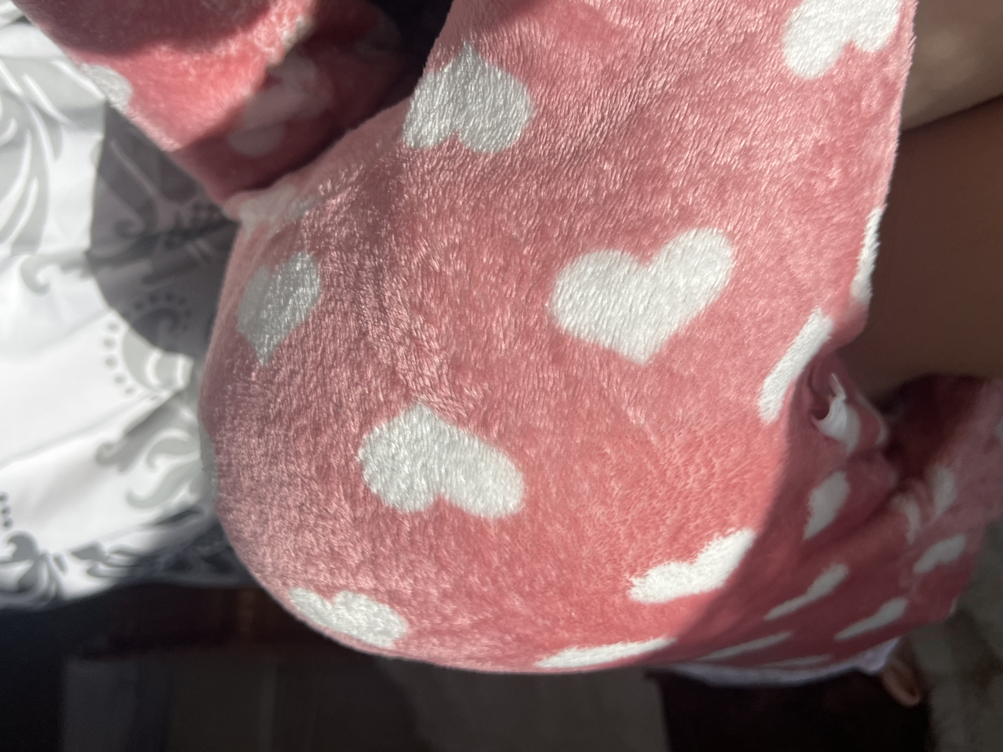 The image shows a close-up of pink, fuzzy fabric with white heart patterns. Part of a white and grey patterned fabric is visible in the background. The location in the city of Elena, Bulgaria cannot be determined from this image.