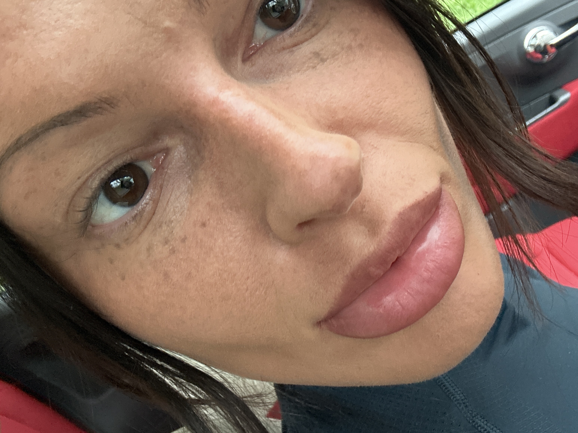 A close-up photograph shows a woman's face. She has brown eyes, dark brown hair, freckles, and pale lips. A car door handle and red interior are partially visible in the background. The location in Tunbridge Wells, United Kingdom cannot be determined from the image.