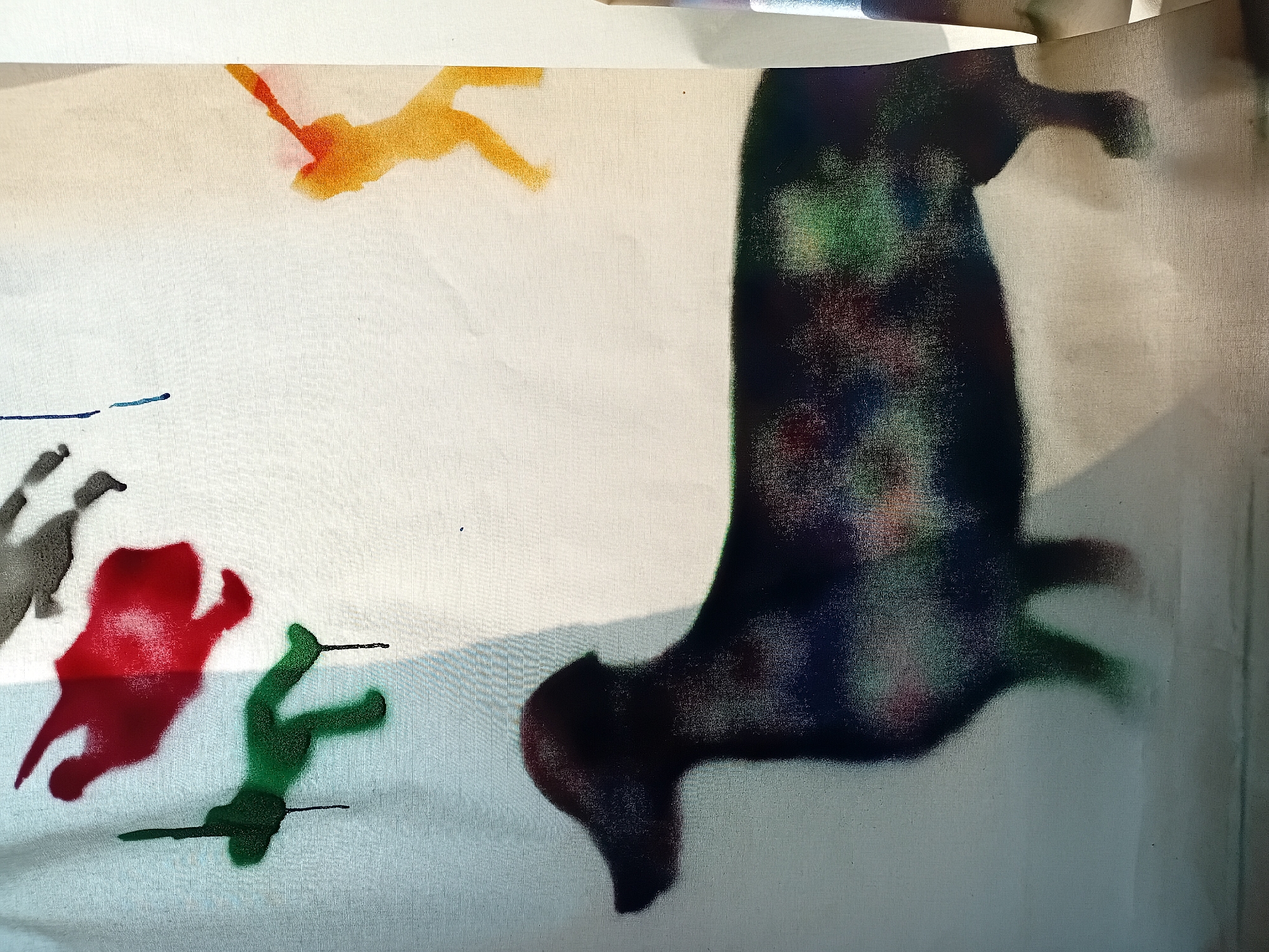 The image displays a white curtain with spray-painted figures. In the upper left, there is a red silhouette of a human figure in mid-air, and below it, a green silhouette of a human figure. To the right of the red figure, a gray silhouette of a human figure is partially visible. In the upper right, an orange silhouette of a human figure is seen, with a red streak extending from its arm. Dominating the lower half of the curtain is a large black silhouette of a dachshund, its body filled with colorful splotches of red, green, and blue. The curtain is illuminated by light, casting shadows and highlighting the texture of the fabric. The backdrop appears to be an indoor setting, possibly a room or a studio, with a bright, undefined area to the right. There is no indication or context suggesting the location is Akhasheni, Georgia.