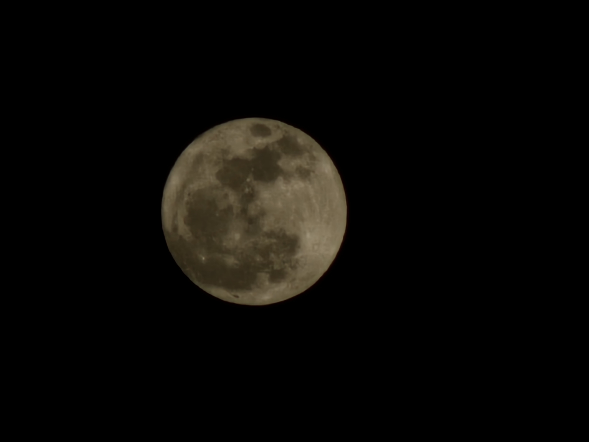 A full moon is prominently displayed against a black background, filling the center of the image. The moon's surface exhibits a textured appearance with visible craters and darker maria, suggesting it is a close-up shot. The lighting on the moon is soft, casting no harsh shadows. The overall composition is simple, with the moon as the sole subject. There is no indication of the city of Tyrnyauz, Russia, or any other environmental details in the image.