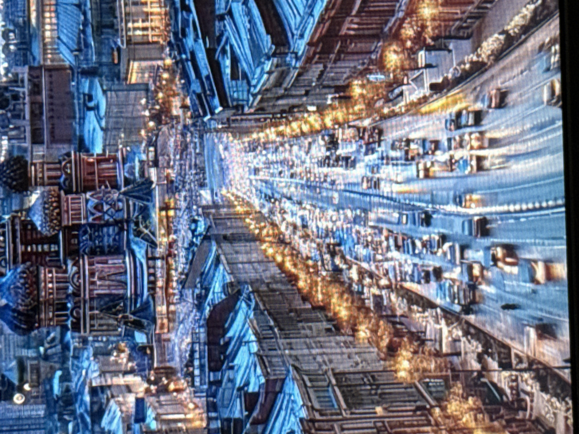 The image is an aerial view of a city street at dusk or night, lined with buildings and filled with traffic. In the background, a prominent structure with colorful, onion-shaped domes, characteristic of Russian architecture, is visible. The street is congested with cars, their headlights and taillights creating streaks of light. Pedestrians are also present on the sidewalks. The buildings on either side of the street have illuminated windows, and streetlights cast a warm glow. The overall scene depicts a busy urban environment. The prompt states the location is in the city of Pushkino, Russia.