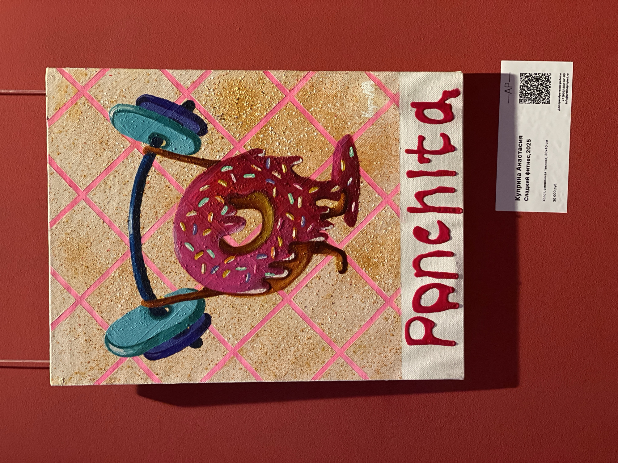 The image shows a close-up of a piece of artwork displayed in what seems to be an exhibition space. The artwork consists of a canvas featuring a drawing of a donut combined with fitness equipment; the donut appears to be lifting weights. The background of the image features a lattice pattern in pink. The title of the artwork, "Panchita," is displayed vertically along the right edge of the canvas in red lettering. A label on the top right, written in Russian, identifies the artist as Kupriyina Anastasiya, the artwork as "Sweet Fitness" (Сладкий фитнес), and the year 2025. It also indicates the medium as mixed media on canvas, with dimensions of 30x40 cm, and a price of 30,000 rubles. A QR code and contact information for purchasing the artwork are also present on the label. The artwork hangs on a red wall. Given the details on the label, the location is likely Moscow, Russia.