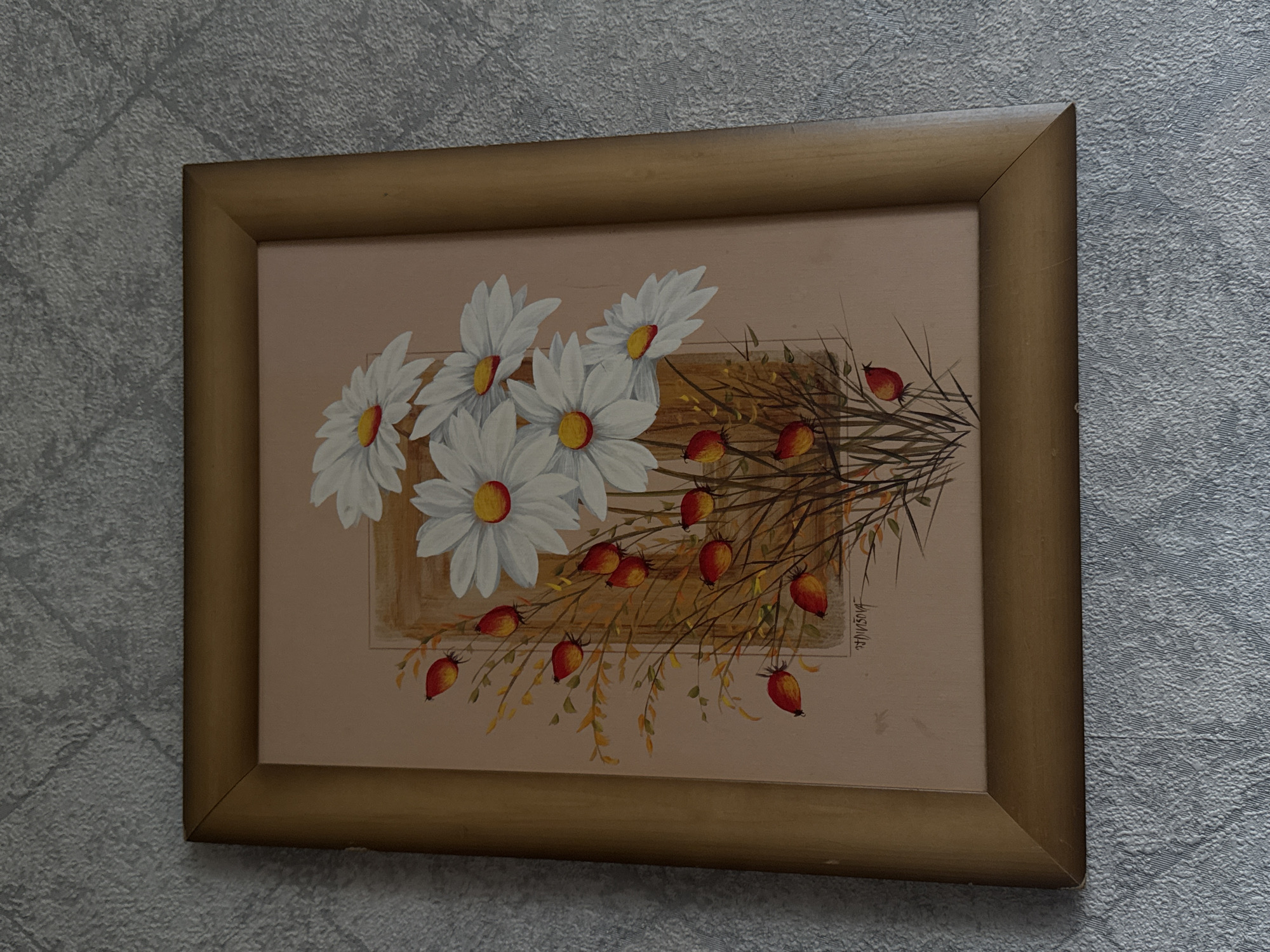 A framed painting of white daisies with yellow centers and red berries hangs on a textured, light gray wall. The painting depicts a bouquet of daisies clustered on the right side, with thin, dry stems and leaves. Several red berries are scattered among the stems. A vertical, light brown rectangular element is present in the center of the painting behind the flowers. The painting is enclosed in a thin, golden-brown wooden frame. The wall on which the painting hangs has a rough, fabric-like texture. The image is a photograph taken from a slightly elevated angle. The painting is signed in the lower right corner with the name "H. Dinsdova". There is no indication of the location of Kholmsk, Russia in this image.