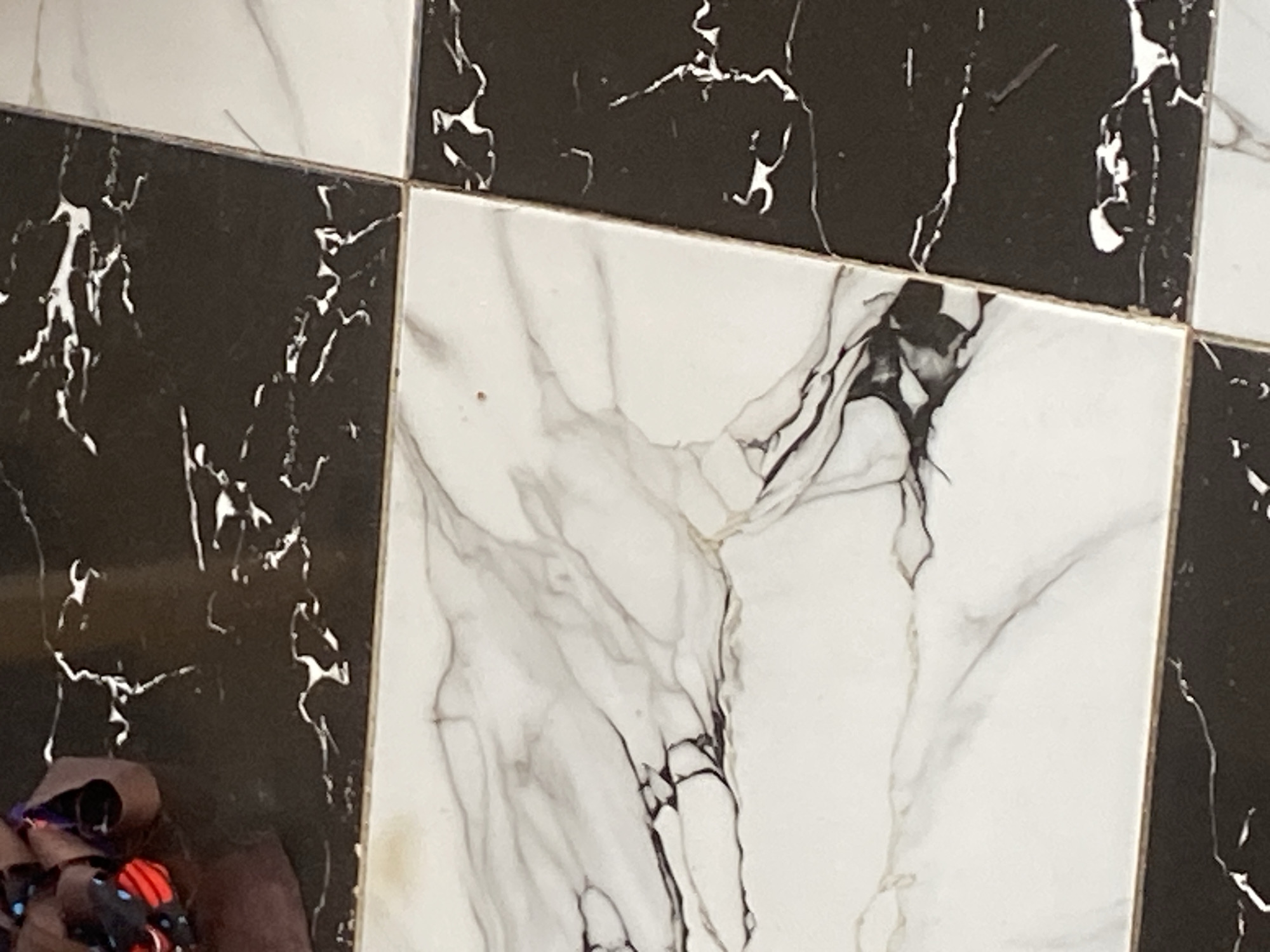 The image shows a close-up view of a checkered floor made of large square tiles. The tiles have a marble pattern, with some being black with white veining, and others being white with black and grey veining. The floor is clean and appears to be indoors. There are no people or animals visible in the image. The scene does not provide any specific geographical or location information that would suggest it is in Jauro Yinu, Nigeria.