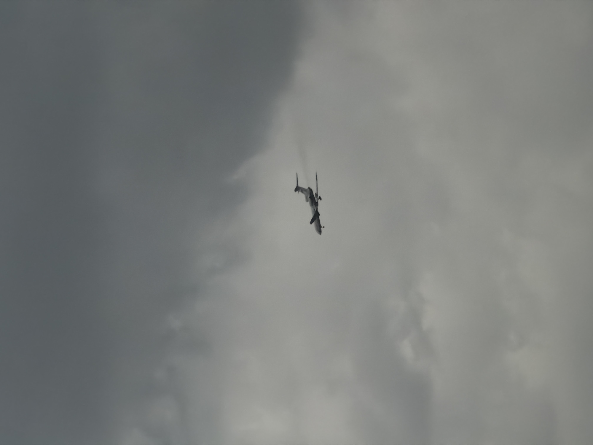 An aircraft flies in the sky. The sky is cloudy and grey. The location is unknown.