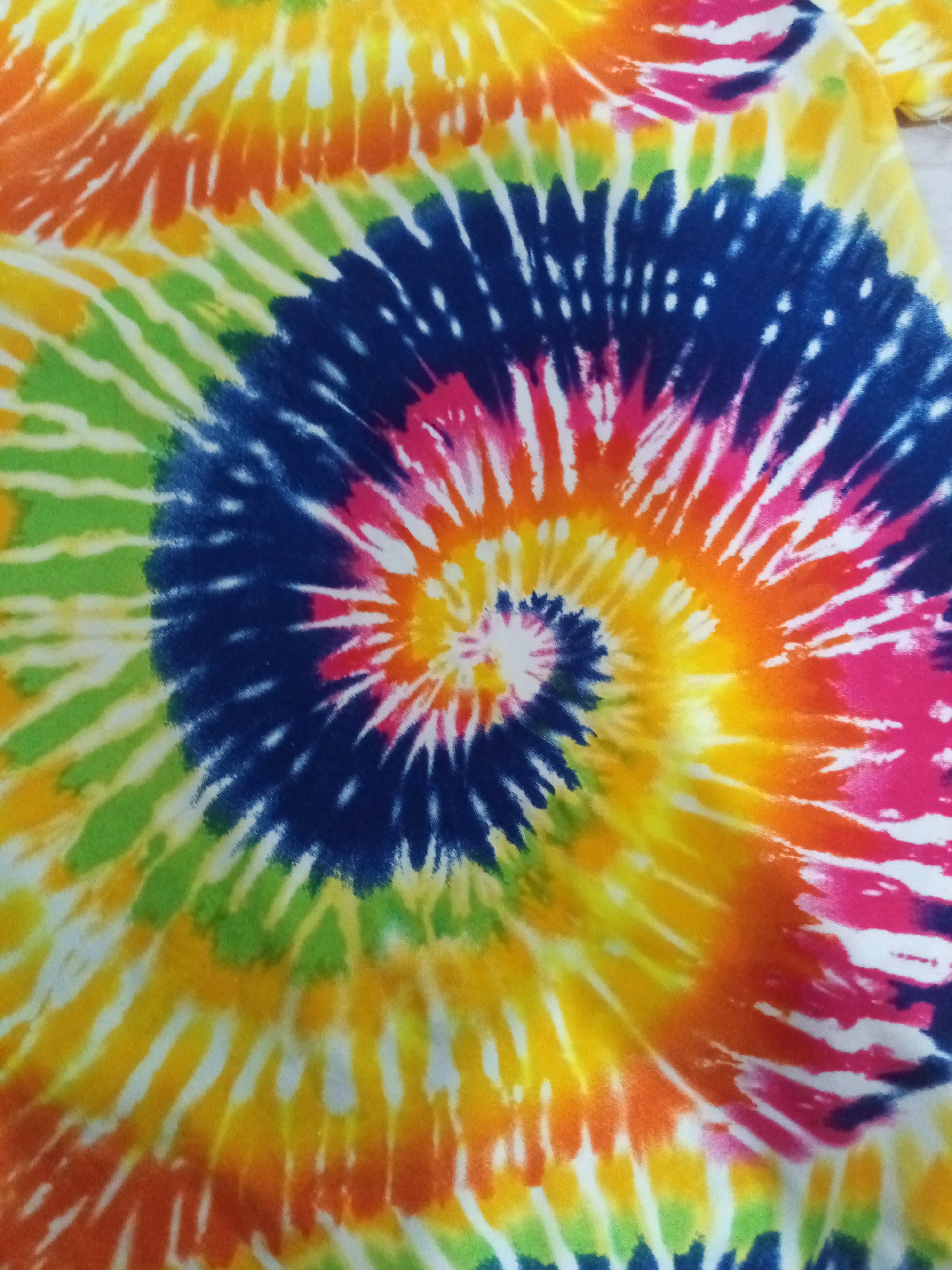 The image shows a colorful tie-dye pattern with a central spiral design. The colors include yellow, orange, pink, blue, and green. White lines separate the different colors. There is no evidence to suggest that the image was taken in Davao City, Philippines.