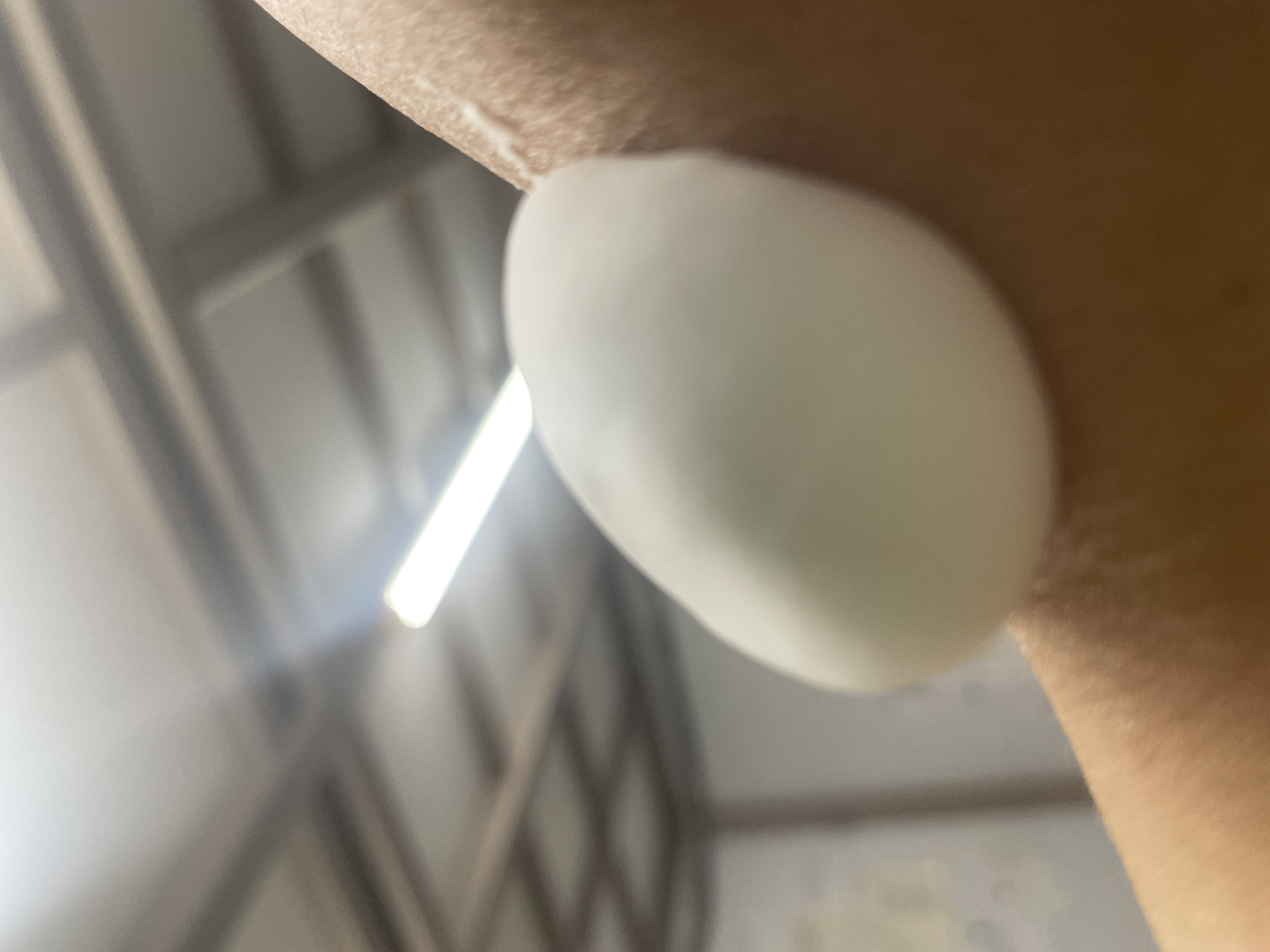 A close-up shot shows a white blob of lotion or cream on a person's skin. The background is out of focus, showing a ceiling with fluorescent lights and a criss-cross pattern of beams, possibly in a warehouse or industrial setting in Tervolovo, Russia. The focus is entirely on the skin and the white substance.