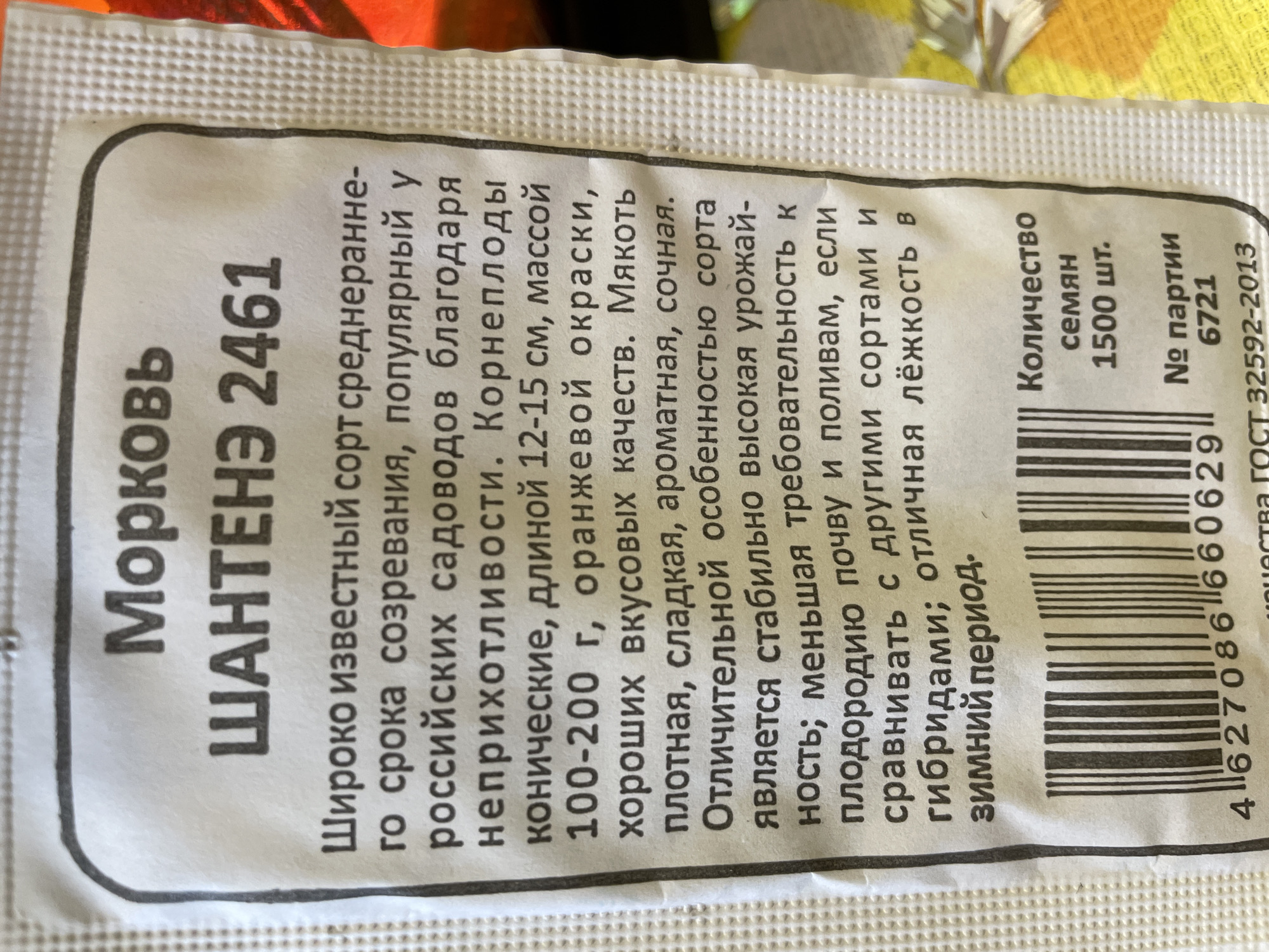 This is a close-up image of the packaging for "Shantené 2461" carrot seeds. The text is in Russian and describes the carrot variety as being widely known, medium-early ripening, and popular among Russian gardeners due to its unpretentiousness. The carrots are conical, 12-15 cm long, weigh 100-200 g, and are orange. The packaging indicates that there are 1500 seeds in the package, with the batch number 6721. A barcode is visible at the bottom of the package, alongside the number "4627086660629". The quality standard GOST 32592-2013 is also printed. The text contains information about the variety's qualities, such as dense, sweet, and juicy flesh, as well as its high yield, lower soil fertility requirements, and good storability in winter. There is no explicit information about the location within Talmenka, Russia, but it could be implied that the seeds are intended for use in that region.