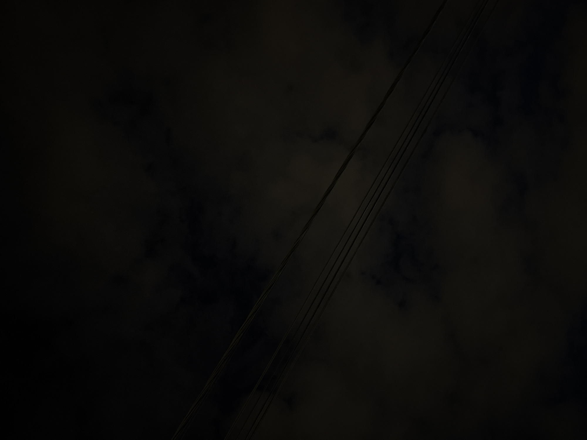 The image is a low-angle shot of power lines against a dark, cloudy sky, likely taken at night or in low light. The power lines run diagonally across the frame from the lower left to the upper right. Faint cloud formations are visible in the background. Location is indeterminate, but it is said to be Belgrade, Serbia.