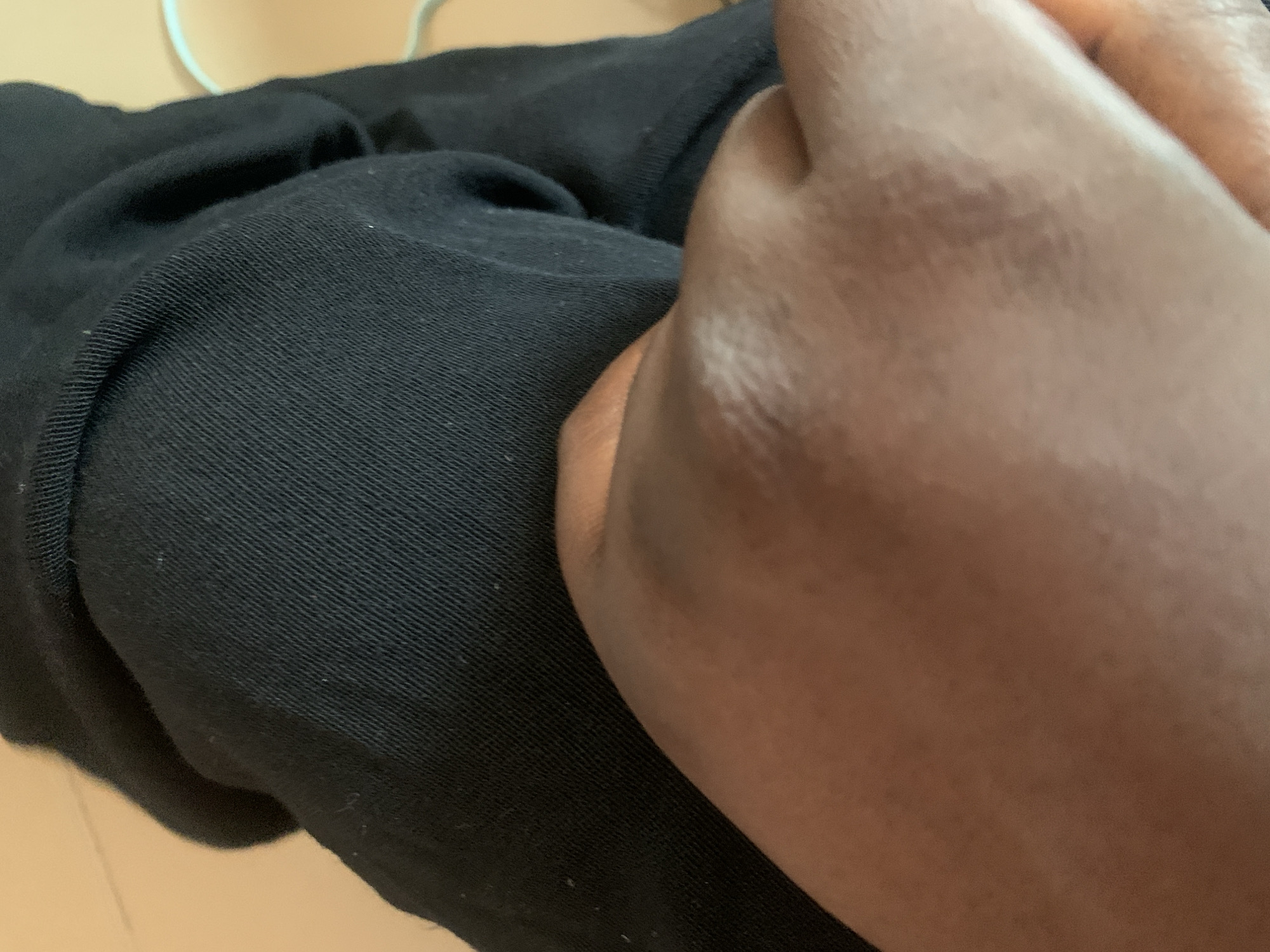 The image is a close-up, low-angle shot of a person's knee and thigh covered by black fabric. The skin on the knee appears to have some texture and is a medium brown color. The fabric is ribbed and drapes in soft folds. The background is a blurry, light orange or beige color, suggesting an indoor environment. There is no discernible indication of the location being in Jauro Yinu, Nigeria.