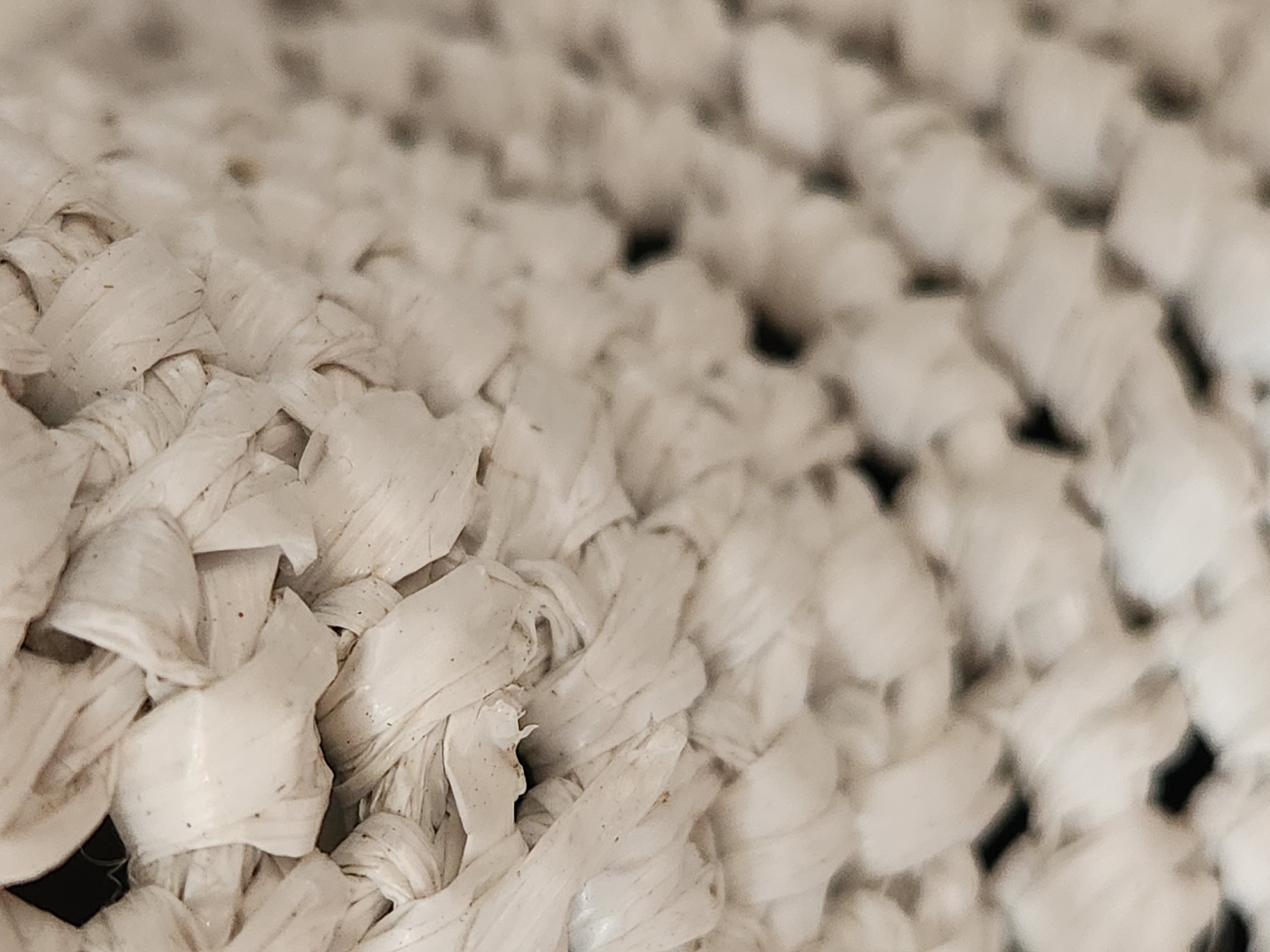 The image shows a close-up, abstract view of a white woven material, possibly a basket or a textured fabric. The weave consists of thick, twisted strands that create a series of interconnected loops and patterns. Some strands appear slightly frayed or worn. The lighting creates shadows within the weave, adding depth and dimension to the texture. The background is out of focus and appears to be dark. There is no discernible location in the city of Maitland, United States of America, nor any people, actions, or interactions present in the image.