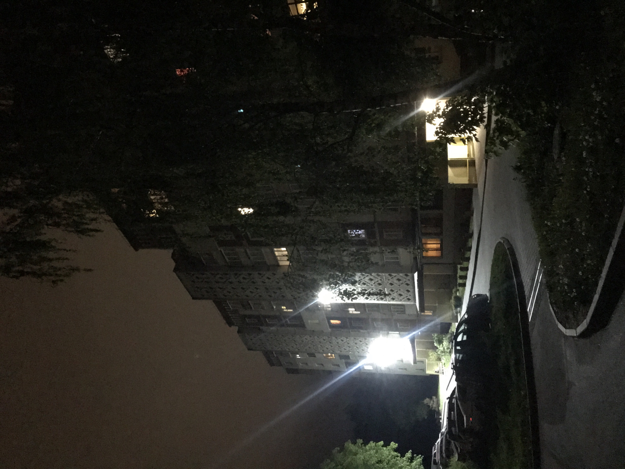 A nighttime view of a residential area in Ternopil, Ukraine, shows a multi-story apartment building with lit windows against a dark sky. A street with trees and vegetation runs alongside the building. Streetlights illuminate the scene. Cars are parked along the street.