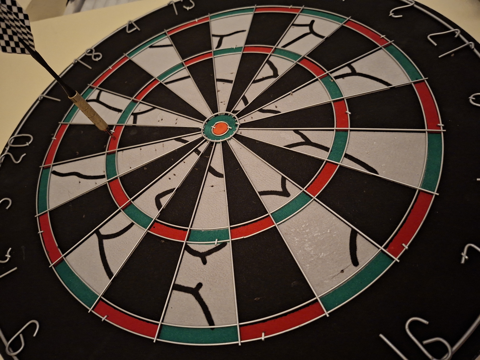 The image shows a dartboard with a dart stuck in the triple 20 section. The dart has a checkered flight and a metallic barrel. The dartboard is a standard design with alternating black and white sections. The numbers indicating score values are visible around the edge. The background is blurry. The dartboard is not recognizable as being located in Plovdiv, Bulgaria. There is no other person in the image.