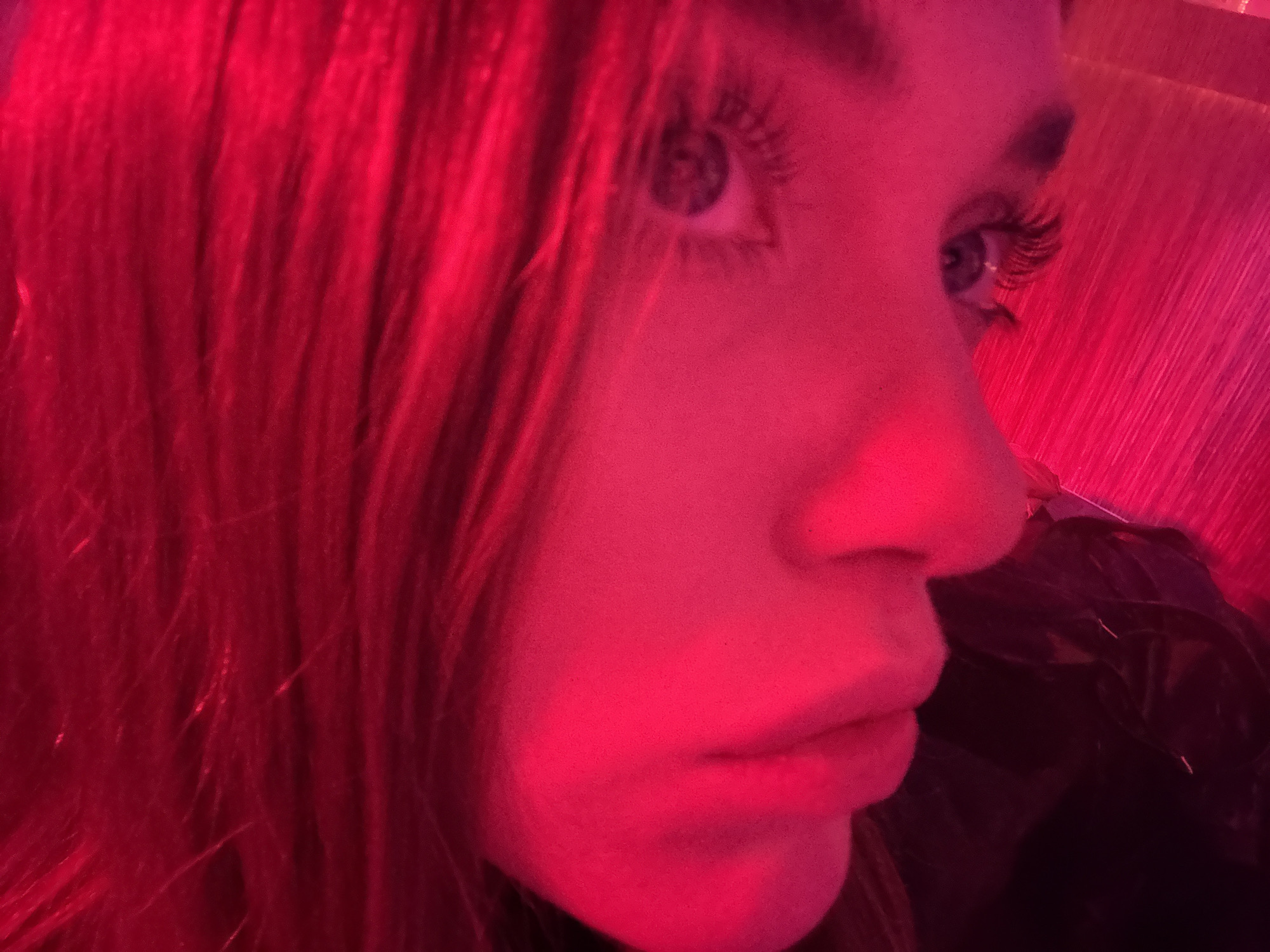 A close-up, medium-shot, low-angle photograph shows a person's face from the side with a strong red light source dominating the scene. The person has fair skin and light eyes, with visible eyelashes. The person’s face is partially framed by what appears to be red hair or possibly a similarly colored background. The red light obscures details, but a nose, lips, and an eye can be seen. The person is likely inside. The location, Mexico City, Mexico, is not possible to determine from the photograph.