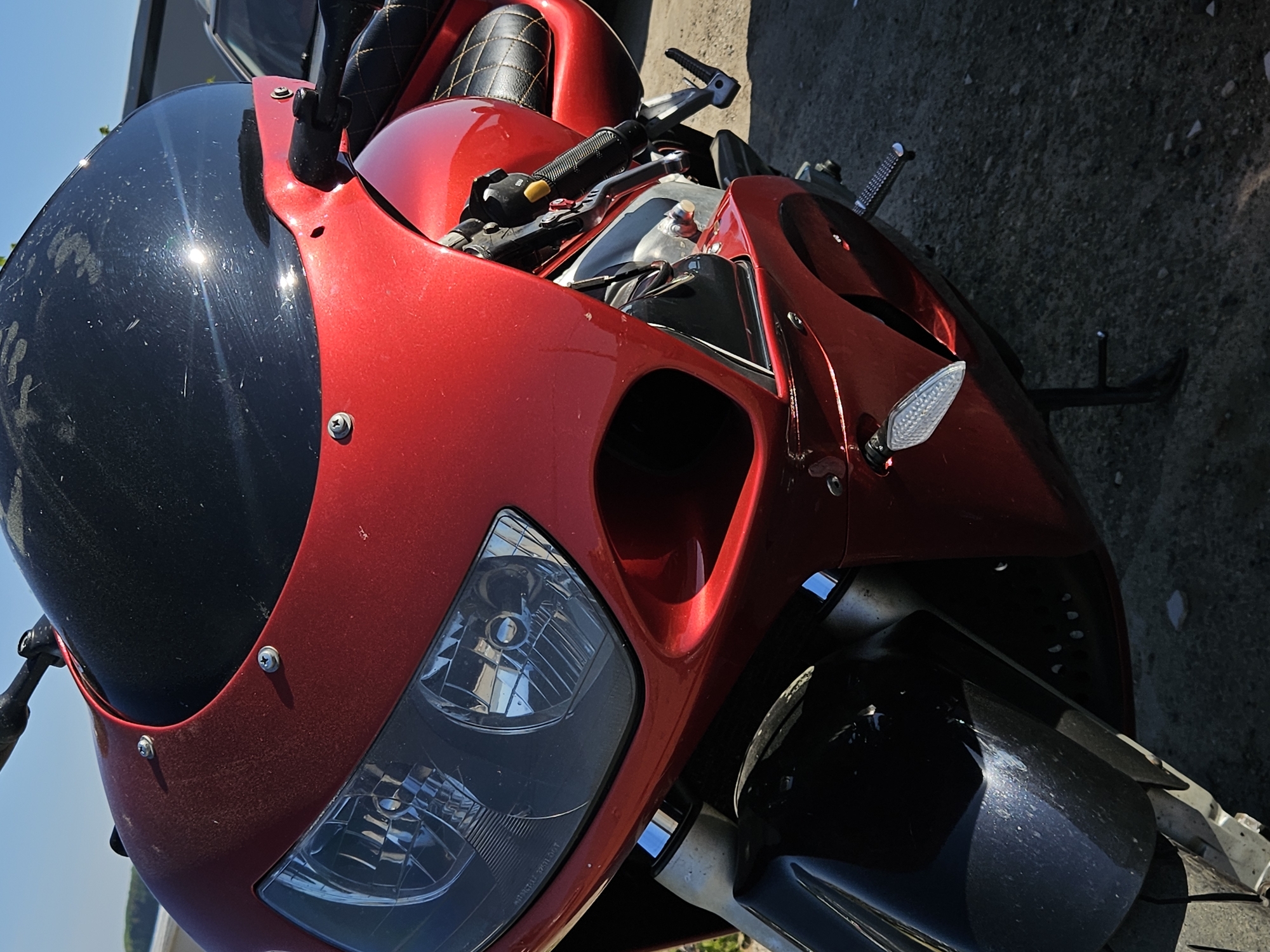 A close-up shot shows a red motorcycle parked on a paved surface. The motorcycle has a black windshield and headlight. The location is not identifiable as being in Chaikovsky, Russia from the given image.