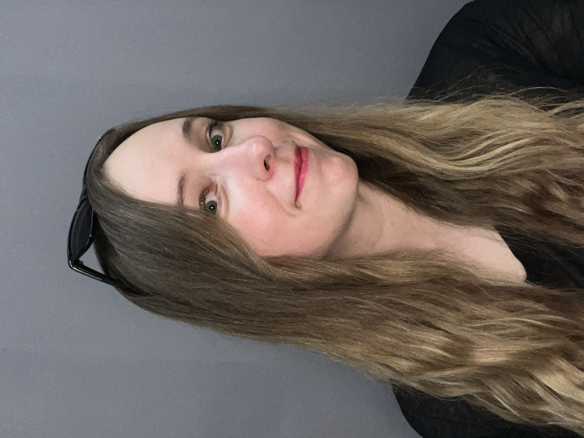 A woman with long, light brown hair poses against a solid grey background. She is wearing a black top. Sunglasses are perched on her head. The image does not provide information about the city of Mytishchi, Russia.
