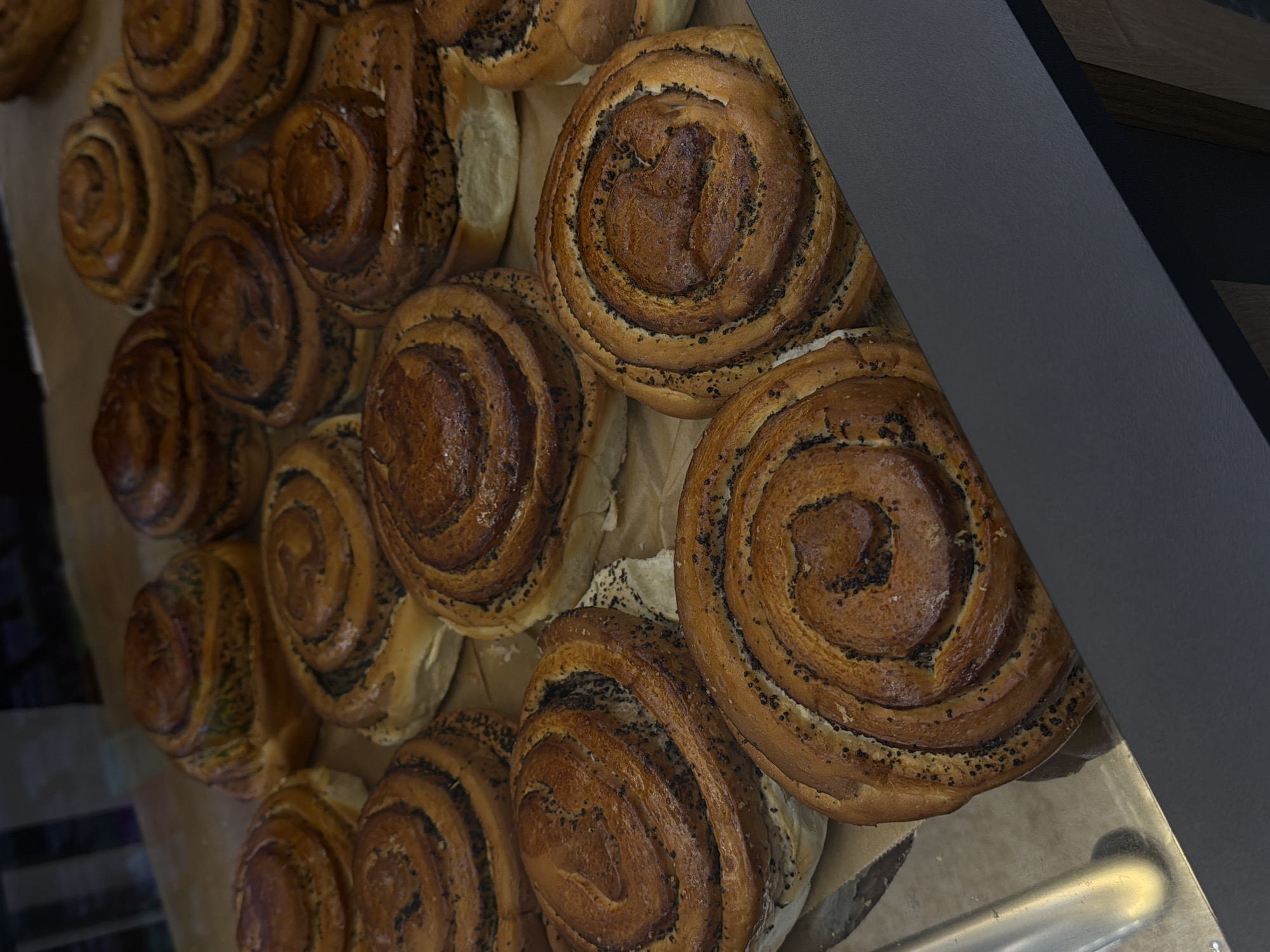 A close-up shot captures a cluster of pastries, likely poppy seed rolls, arranged on a surface that appears to be lined with parchment paper. The rolls are circular, showcasing a spiraled filling that contrasts with the golden-brown crust. Some rolls are partially obscured by a dark gray, presumably metal or plastic, barrier, suggesting they are displayed within a pastry case. The photograph is probably taken indoors, possibly in a bakery or cafe. While the information to identify the location as Yerevan, Armenia is unavailable, it is likely these are freshly baked pastries displayed for sale.