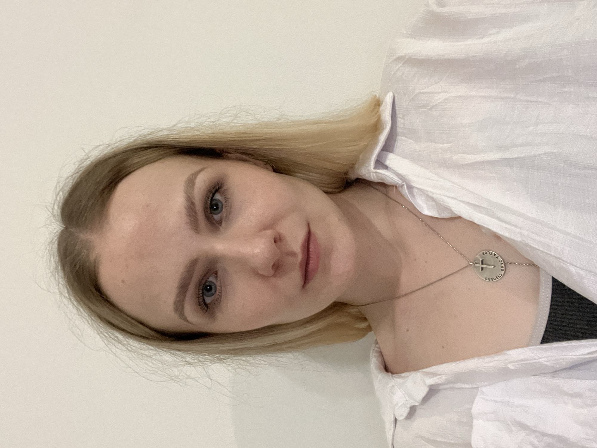 A woman with blonde hair, wearing a white shirt and a silver necklace with a cross pendant, is posing for a photo against a plain white background. The image does not depict Khimki, Russia, nor does it provide any information to ascertain the location.