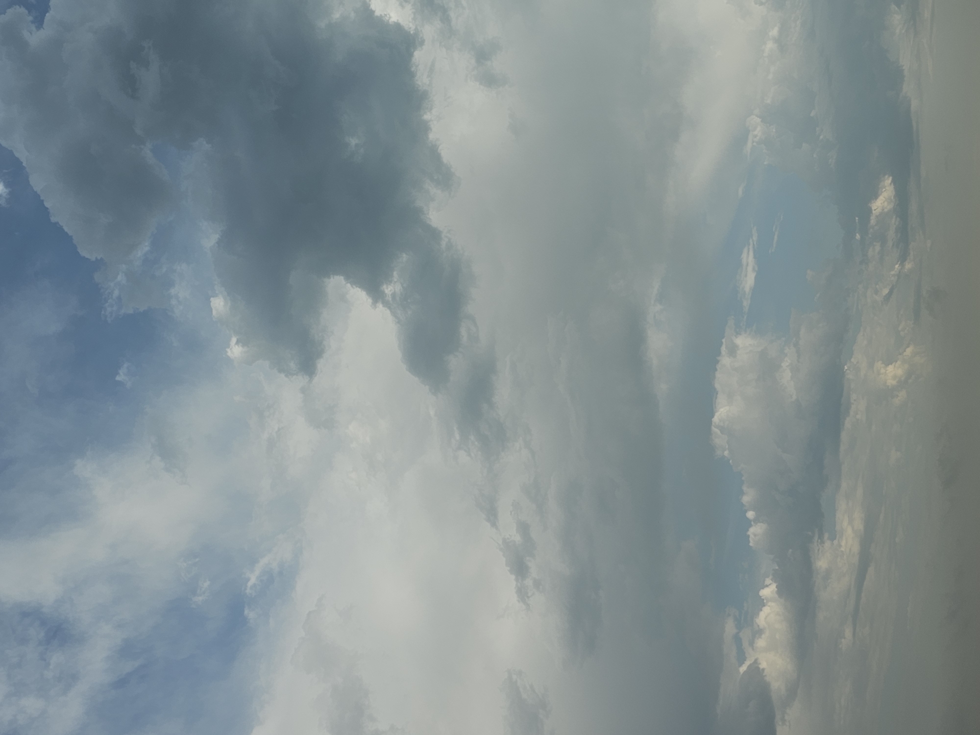 The image depicts a cloudy sky with varying densities of clouds. The clouds range from bright white and wispy cirrus formations to darker, more substantial cumulus and cumulonimbus clouds. Patches of blue sky are visible in between the cloud cover. The lighting suggests it is daytime, possibly late afternoon or early evening, as indicated by the diffused light and the muted colors. There is no discernible evidence of human activity, structures, or natural landscape features in this image, as it solely focuses on the sky. The image does not provide any information to place it in the city of Ob, Russia, or any other specific geographical location.