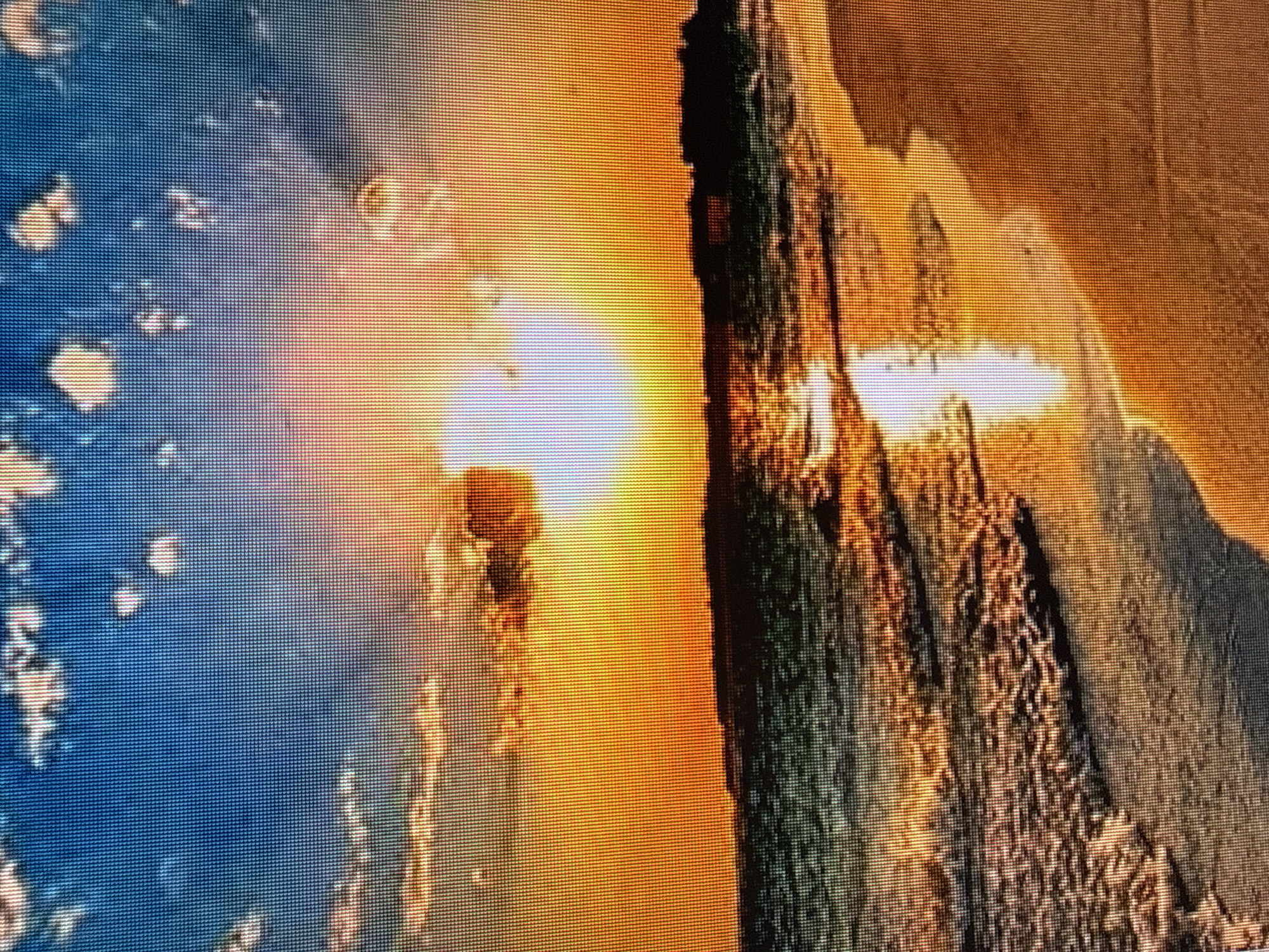 The image displays a digital artwork or a heavily processed photograph depicting a dramatic sunset or sunrise. On the left side, a bright, luminous sun is partially obscured by atmospheric haze, casting a warm, orange glow across the scene. Scattered, lighter-colored shapes, possibly clouds or abstract elements, are visible in the blue-toned background on the far left.
The right side of the image is dominated by a dark, jagged, mountainous or rock-like formation. The texture of this formation is rough and detailed, with highlights of orange and yellow from the celestial light. The overall impression is one of a natural landscape bathed in intense, fiery light. The pixelated nature of the image suggests it might be a display on a screen or a low-resolution digital file. There is no visible text. The scene evokes a sense of awe and natural grandeur, with the intense light and contrasting dark formations creating a powerful visual impact.