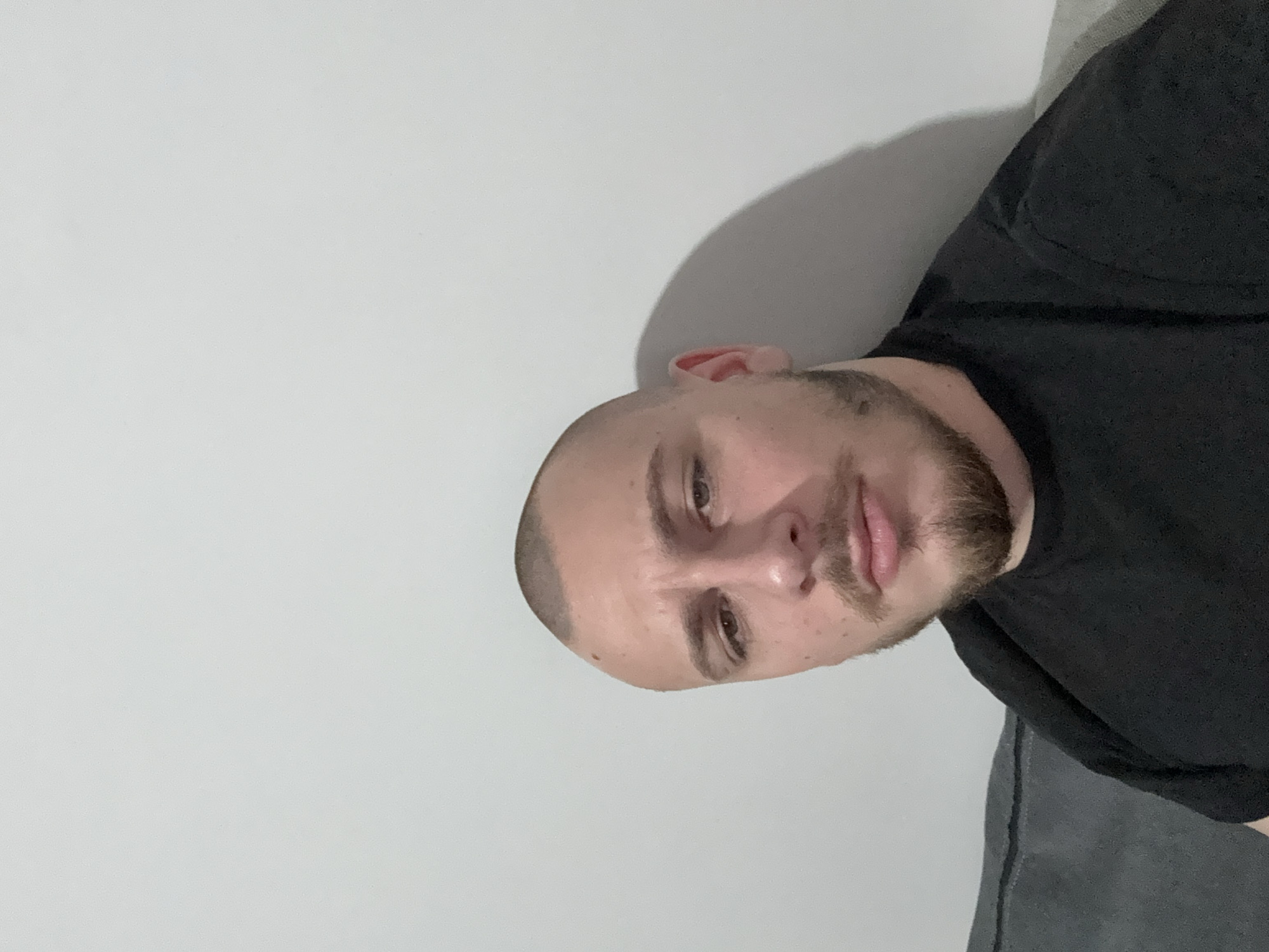 A man with a shaved head and a short beard is shown in a selfie. He is wearing a black shirt. The background is a plain white wall. There is no indication in the image that shows the location of the city of Stara Zagora, Bulgaria.