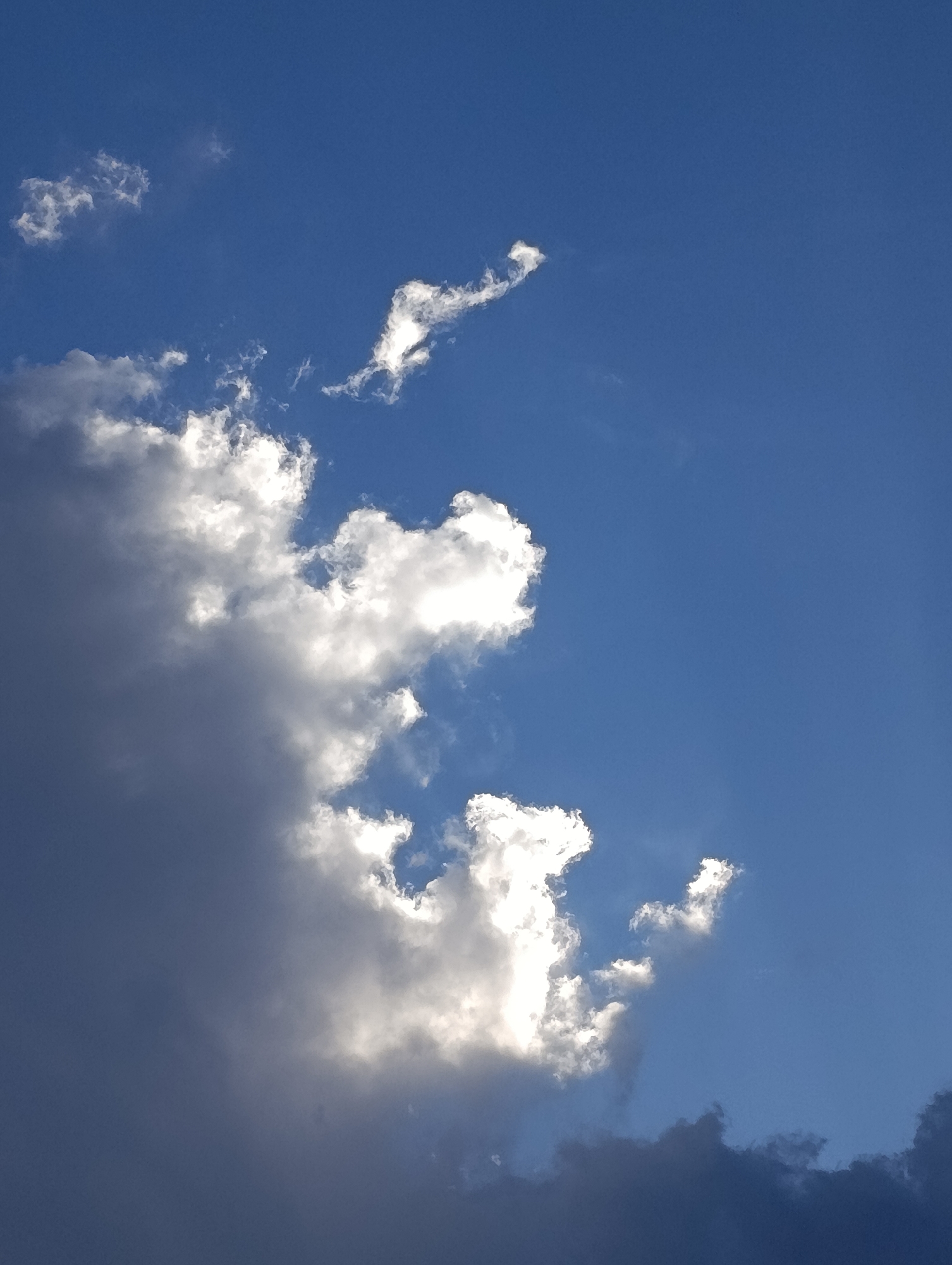 The image shows a view of the sky with clouds. The clouds range from dark gray to bright white, with some appearing to be illuminated from behind. The sky is a bright blue, with some areas appearing darker. There are no people or recognizable objects in the image. The location is not discernible from the image alone, but it is specified as Svilengrad, Bulgaria.