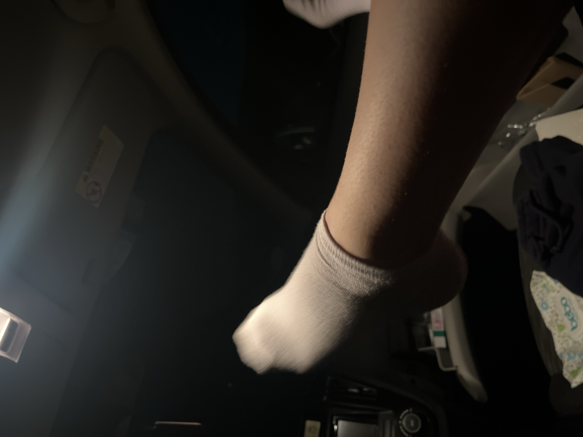 A close-up, poorly lit shot of a person's leg and foot wearing a white sock. The person is seemingly inside a vehicle, based on the dashboard visible in the background. Other objects in the background are vaguely discernable, but not clearly identifiable. The image is taken at night or in a dark environment. No information is available to ascertain if the image location is in the city of Marulevo, Bulgaria.