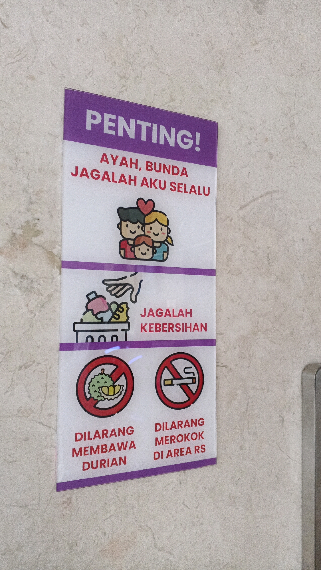 The image shows a sign mounted on a tiled wall, likely in a public indoor space. The sign is divided into three sections, each with a purple border. The top section features the word "PENTING!" (Important!) in large white letters on a purple background, followed by the text "AYAH, BUNDA JAGALAH AKU SELALU" (Father, Mother, Always Take Care of Me) in red. Below this text is an illustration of a family of three smiling. The middle section shows an illustration of a hand throwing trash into a bin and the text "JAGALAH KEBERSIHAN" (Maintain Cleanliness) in red. The bottom section contains two circular red prohibition signs with white borders. The left sign shows a durian fruit with a red cross over it, accompanied by the text "DILARANG MEMBAWA DURIAN" (Forbidden to Bring Durian). The right sign shows a lit cigarette with a red cross over it, accompanied by the text "DILARANG MEROKOK DI AREA RS" (Forbidden to Smoke in the Hospital Area). The wall appears to be made of light-colored, textured tiles. The overall presentation suggests the sign is intended to convey rules or important messages, likely within a hospital or healthcare facility, given the mention of "AREA RS" (Hospital Area). The sign is oriented vertically. The lighting is bright and uniform, indicating an indoor setting with artificial light. The location is specified as Semarang, Indonesia.