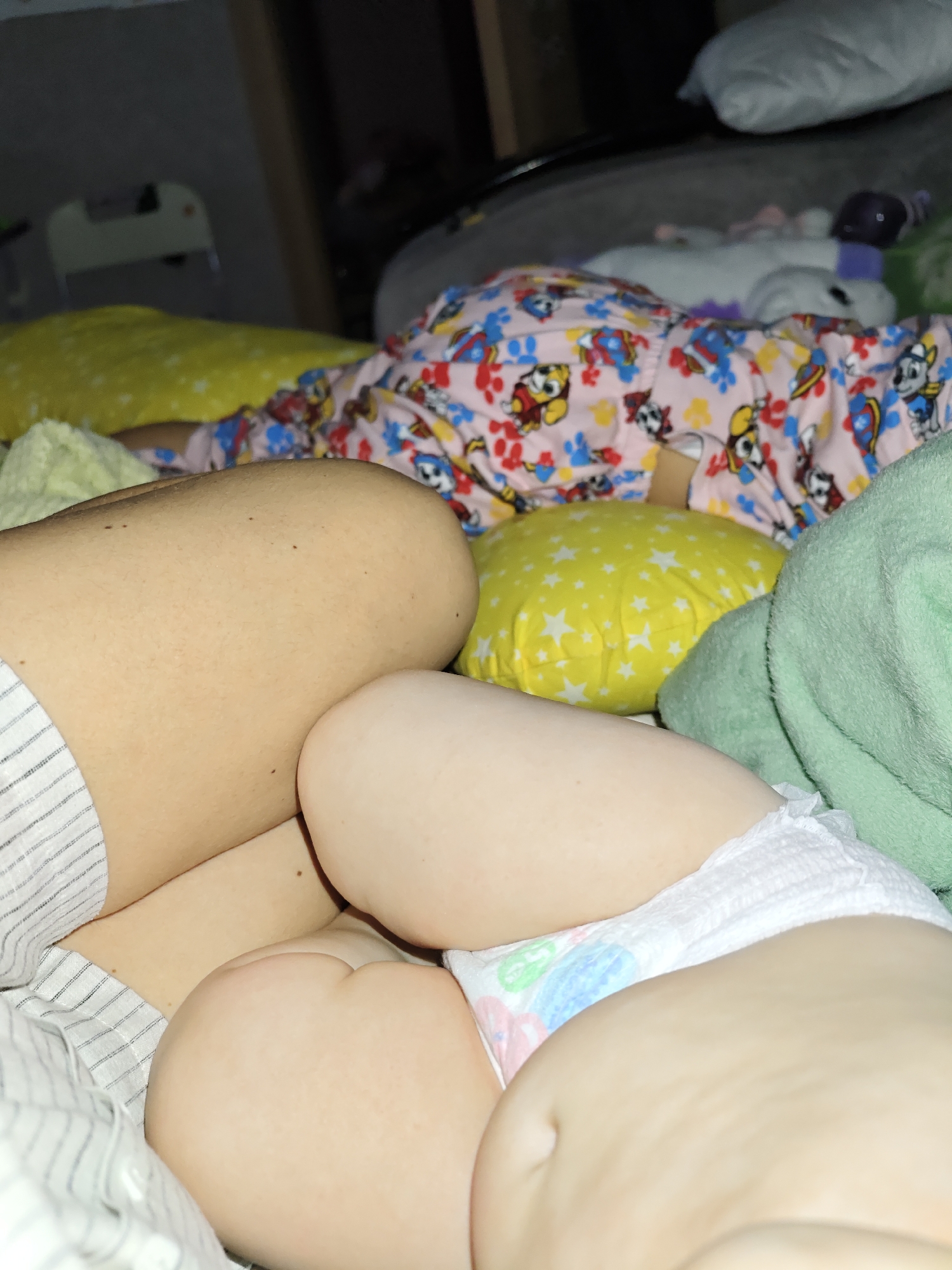A close-up, indoor shot depicts a sleeping child in a diaper, seemingly resting beside an adult. The child's diaper is white with colorful designs. They are also next to a green blanket. The adult appears to be wearing striped pajamas. The location is unknown as it cannot be inferred from the provided image, and therefore, it can not be confirmed that it is in Chaikovsky, Russia.