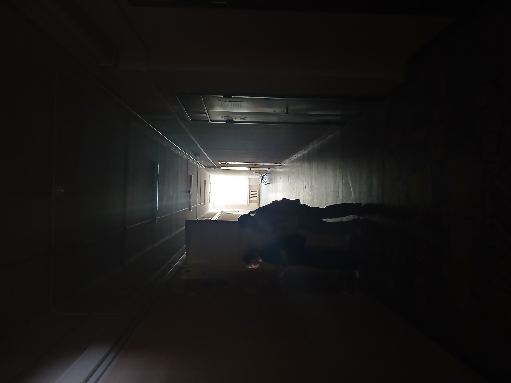 A dimly lit hallway leads to a bright exit. A person stands in the middle ground. The location is Chaikovsky, Russia.