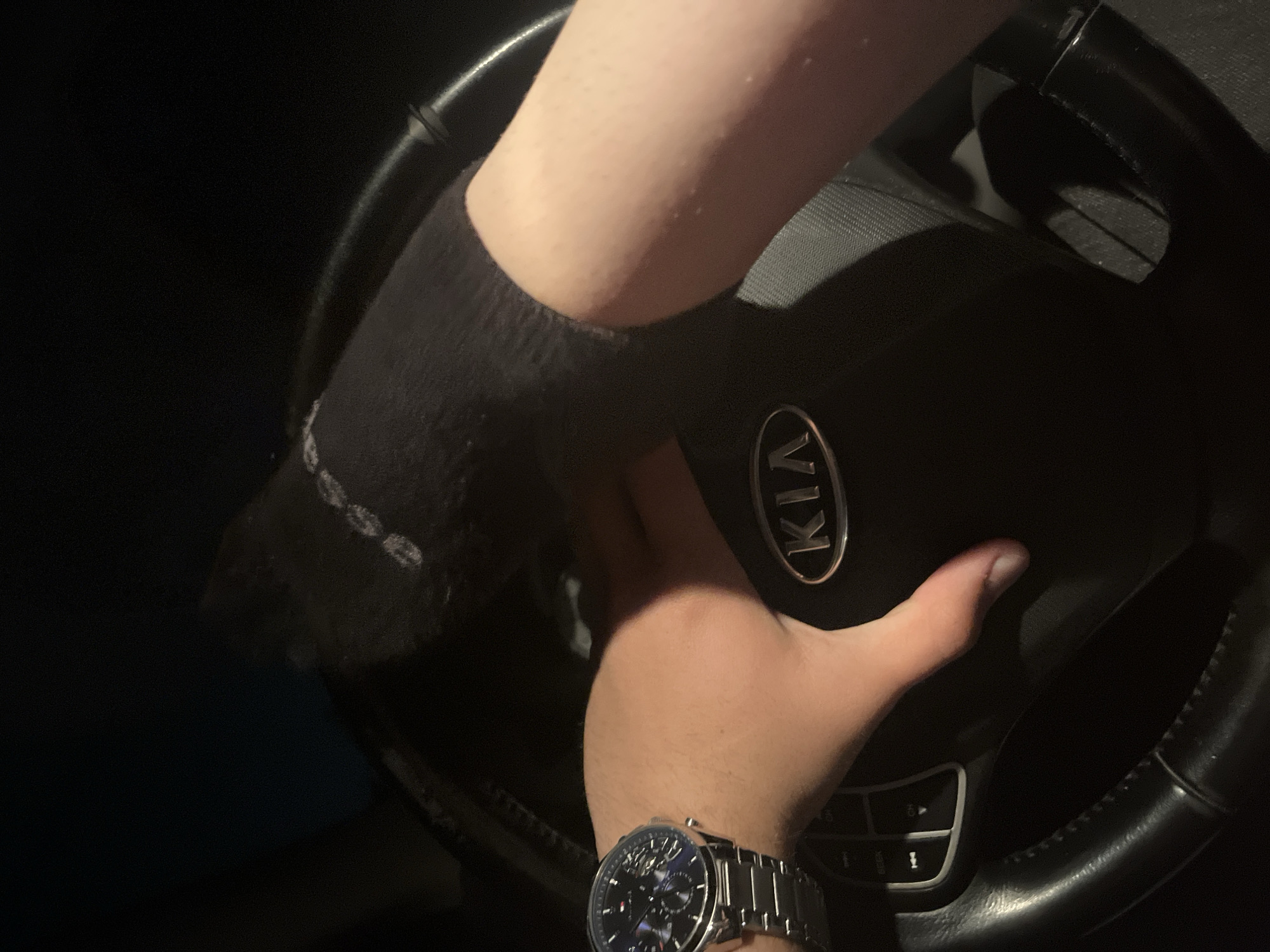 A person is driving a Kia vehicle. The person is wearing a black sock on their right hand and a silver watch on their left wrist. The scene is dark. The city of Marulevo, Bulgaria, is not discernible from the image.