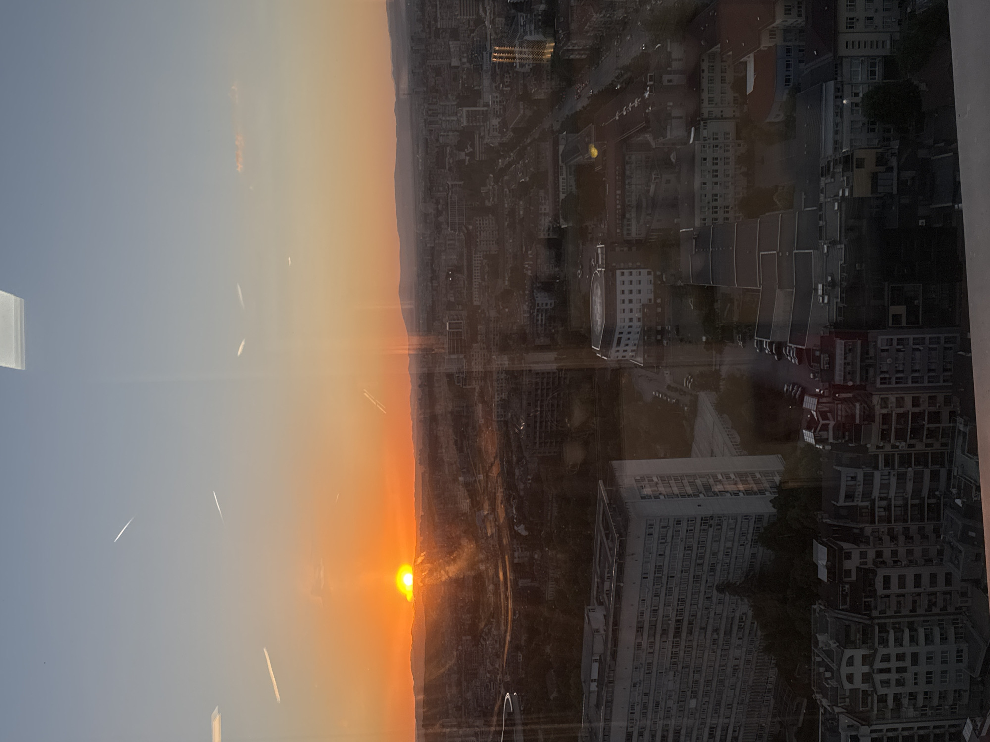 A sunset over Sofia, Bulgaria is viewed through a window. The buildings are visible as are contrails in the sky. The window reflects the image of buildings in the city.
