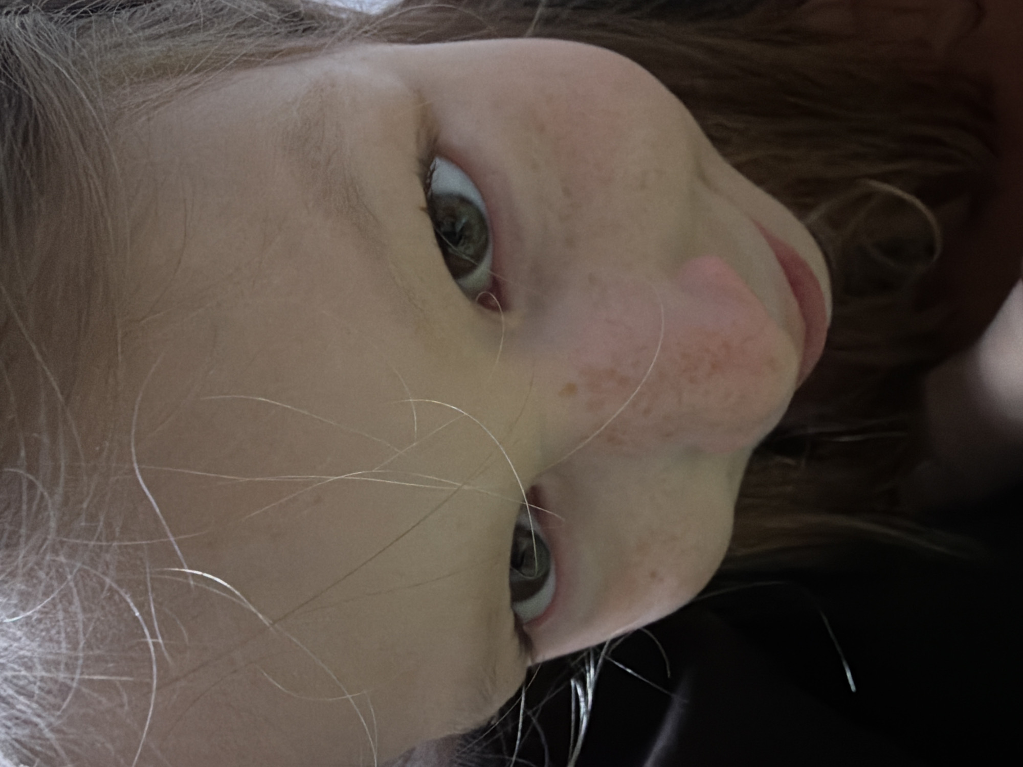 The image depicts the face of a young child with light skin and brown hair. The child has brown eyes and freckles on their nose and cheeks. The background is dark and out of focus. The location is not discernible from the image. No city or environmental markers are visible to indicate Dubovaya, Russia.