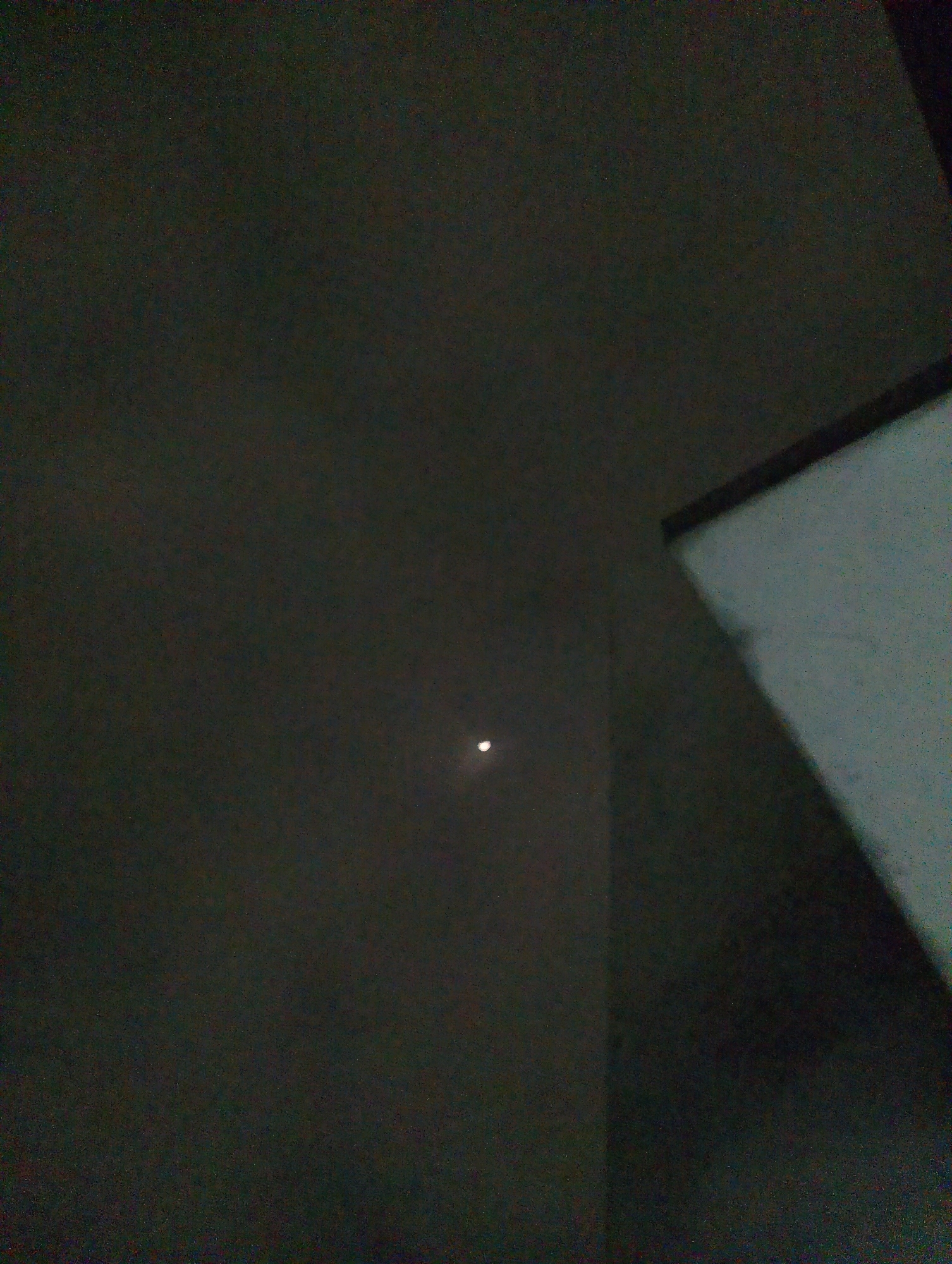 The image shows a dark, somewhat grainy, interior view of what appears to be a room. A single, small, bright point of light, likely the moon, is visible in the upper left portion of the scene against a dark background. To the right, a large, flat, illuminated surface, possibly a screen or projection, casts a shadow. The overall impression is of a dimly lit space, with artificial light from the right contrasting with the faint celestial light from the left. No people, specific objects, or actions are clearly discernible. The location in Magelang, Indonesia cannot be determined from the visual information provided.