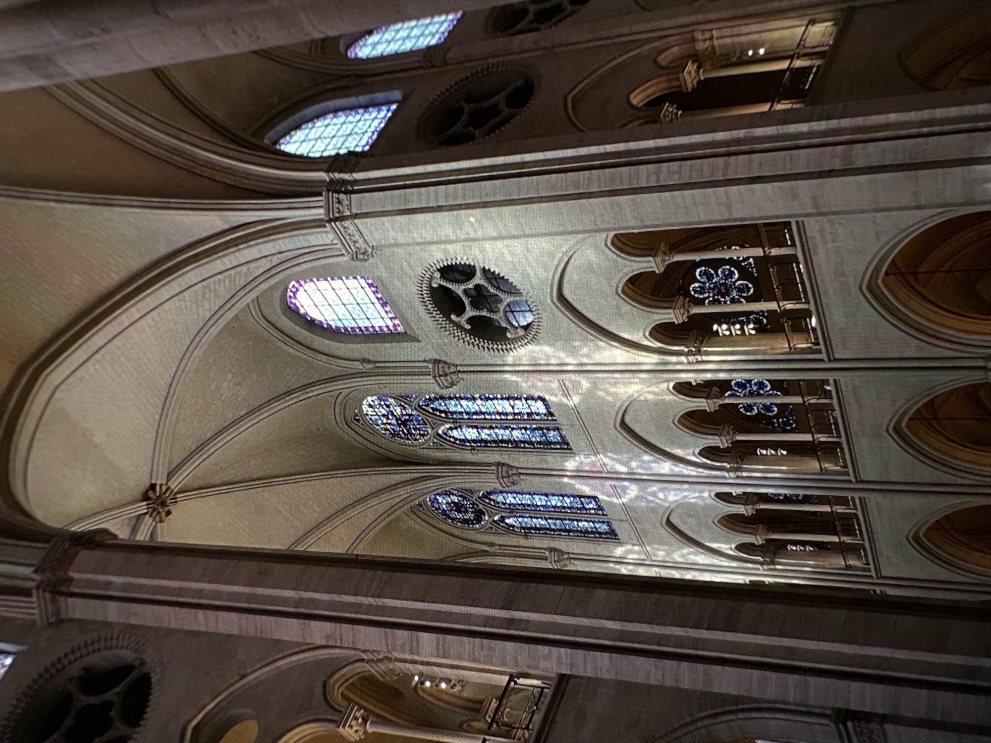 The image shows the interior ceiling of a Gothic-style building, possibly a cathedral. The ceiling features pointed arches, ribbed vaults, stained glass windows, and decorative circular windows with intricate designs. The environment is dimly lit, highlighting the architectural details and stained glass. There are no people visible in the scene. The location, Chișinău, Moldova, cannot be confirmed based on visual information alone.