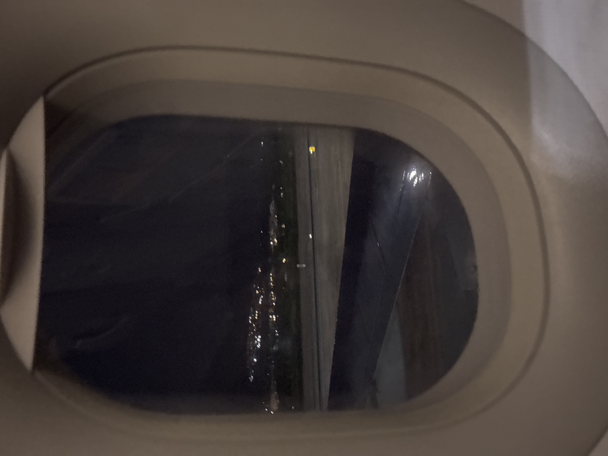 The image shows a view from an airplane window at night. Outside, city lights are visible. The wing of the plane is also visible through the window. It is impossible to determine if the location is Churriana, Spain from the available image.