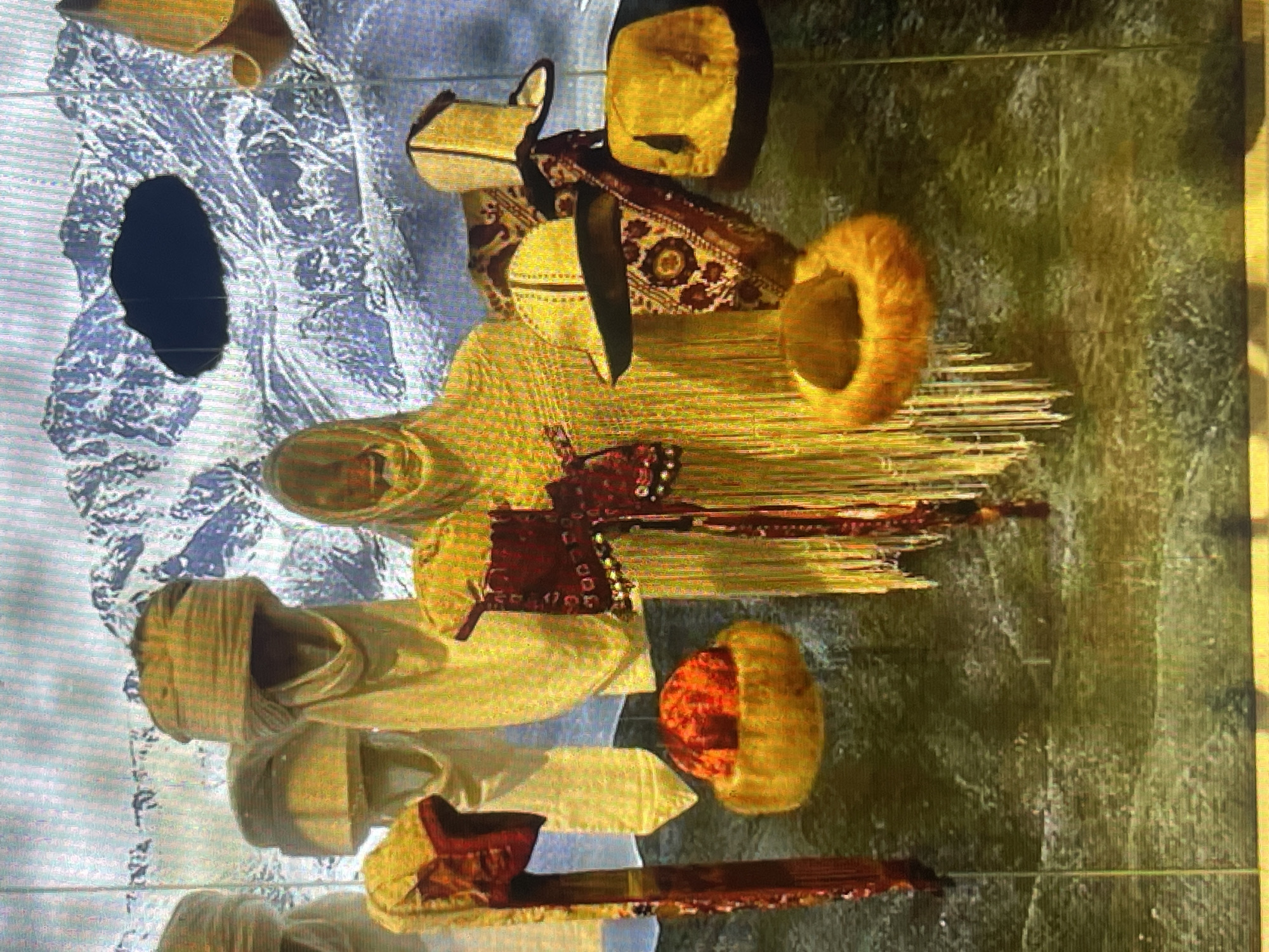 The image depicts a display of traditional headwear, possibly for sale or exhibition, against a backdrop of a snow-capped mountain range. The headwear varies in style and material, with some appearing to be turbans, and others more structured hats, some adorned with fur. The display includes several mannequins or figures draped in flowing garments, likely to showcase the headwear in context. The overall impression is one of cultural display. There is no indication of the city of Bishkek, Kyrgyzstan within the image itself.