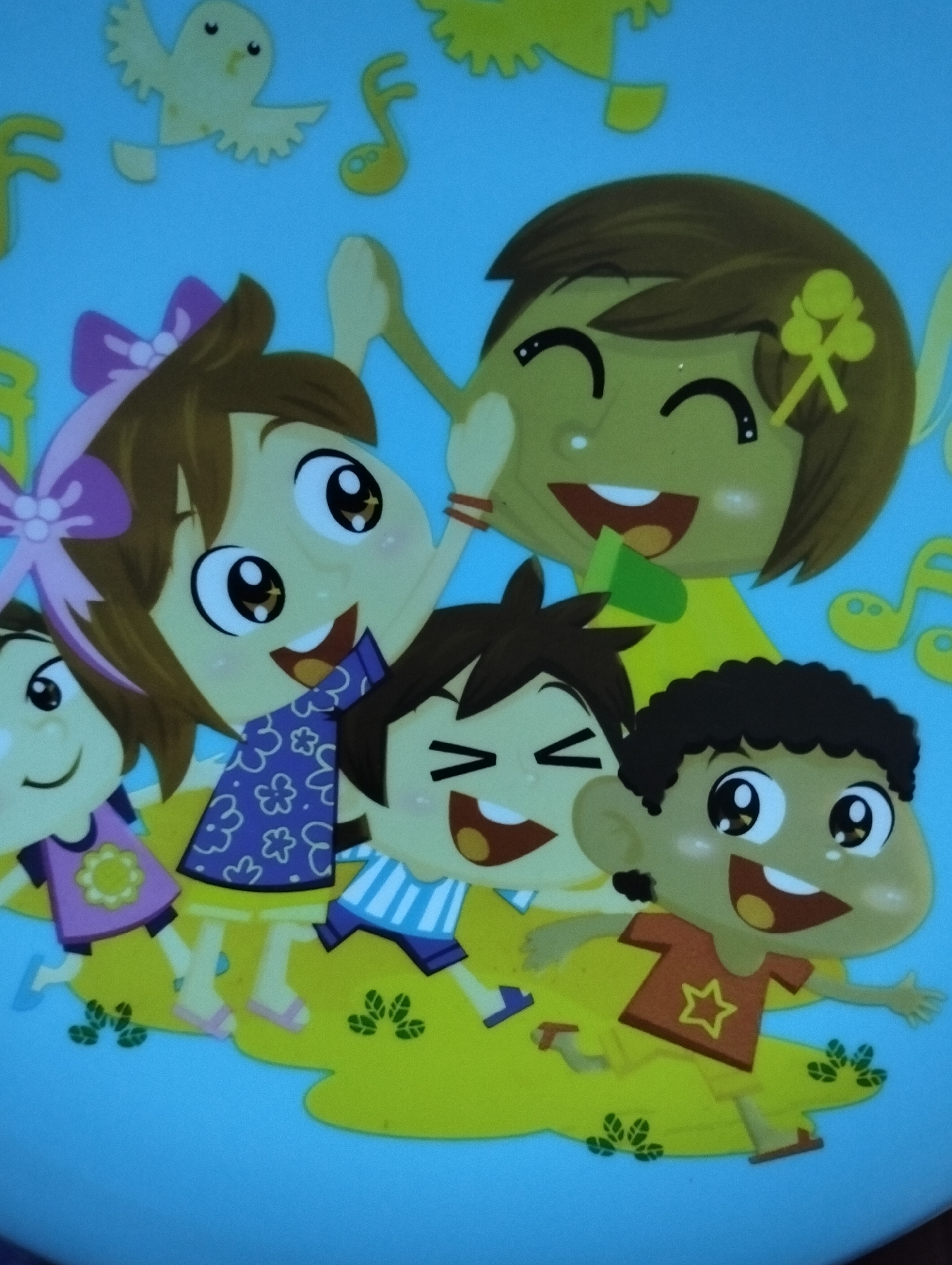 The image is a colorful, cartoon-style illustration featuring a group of diverse children playing on a yellow, grassy surface against a light blue background. A yellow bird with spread wings is depicted in the upper left corner, and musical notes are scattered throughout the background.
From left to right, the children include:
* A child with brown hair and a purple bow, wearing a purple dress with a yellow flower design.
* A child with dark brown hair, wearing a blue and white striped shirt and blue shorts.
* A child with brown hair, wearing a patterned purple and blue top.
* A child with dark, curly hair, wearing an orange t-shirt with a yellow star and yellow shorts.
The children appear to be happy and energetic, with wide smiles and open mouths. Some are reaching out or jumping, suggesting a playful and active scene. The overall style is bright and cheerful, characteristic of children's entertainment or educational materials.
The provided crops focus on different sections of the illustration, highlighting the details of the children's faces, clothing, and some of the background elements. There is no indication of a city location, including Paciran, Indonesia, in the image itself. Therefore, it is not possible to describe the location in Paciran, Indonesia, based solely on this image.