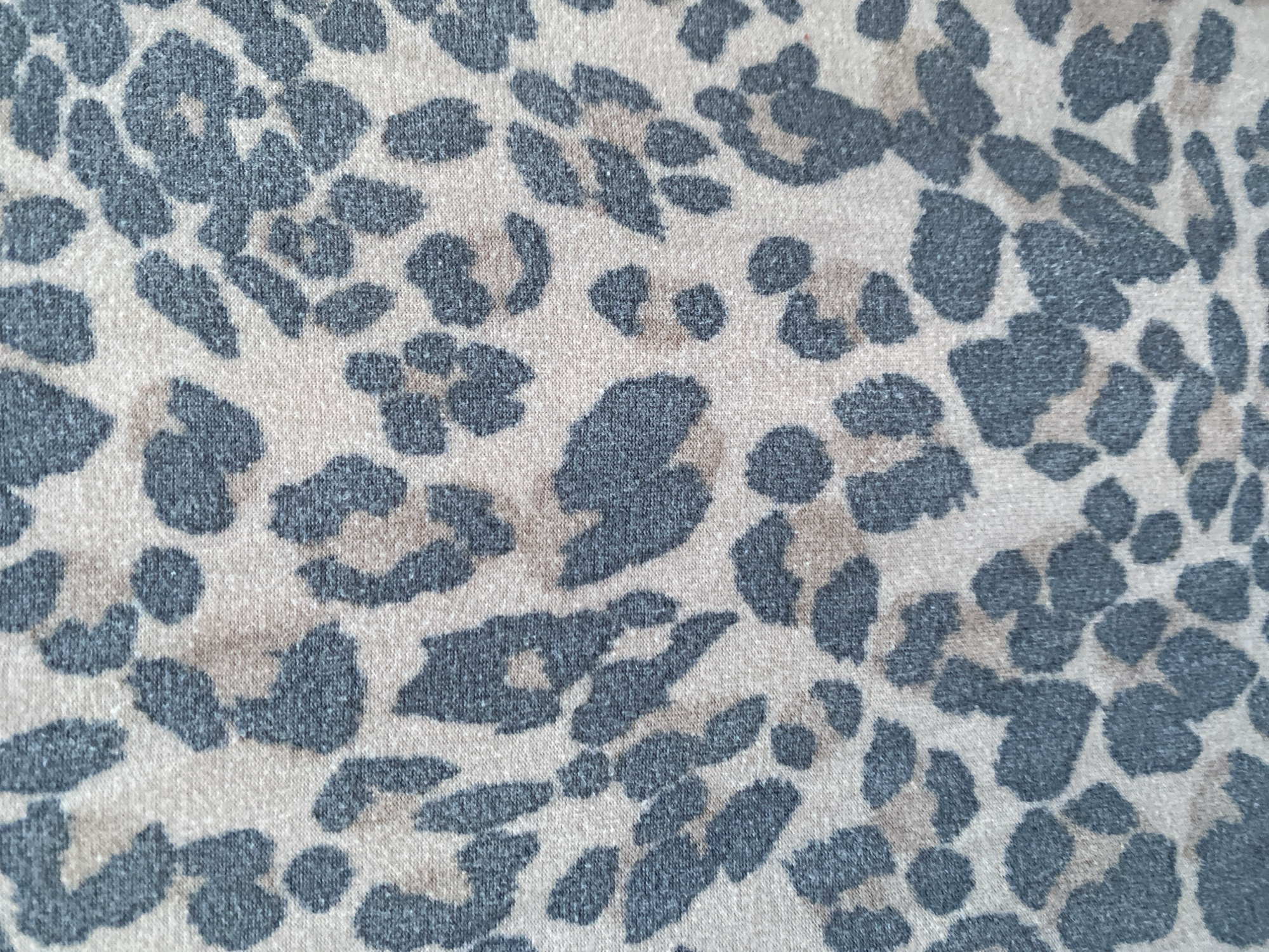 The image displays a close-up, abstract view of a fabric with a leopard print pattern. The pattern consists of irregular, dark grey shapes scattered across a lighter, beige background. The fabric appears to be knitted, with a visible texture of small loops and fibers, suggesting it could be clothing or upholstery. There is no discernible subject, activity, or event taking place; it is a static, patterned surface. No text is visible. The context of Lafia, Nigeria, is provided, but there are no visual cues within the image itself to suggest this specific location. The lighting appears even, indicating it's likely an indoor setting or a well-lit outdoor area without direct sunlight. The colors are muted, with the grey and beige tones creating a somewhat subdued aesthetic. The image is purely focused on the textile design.