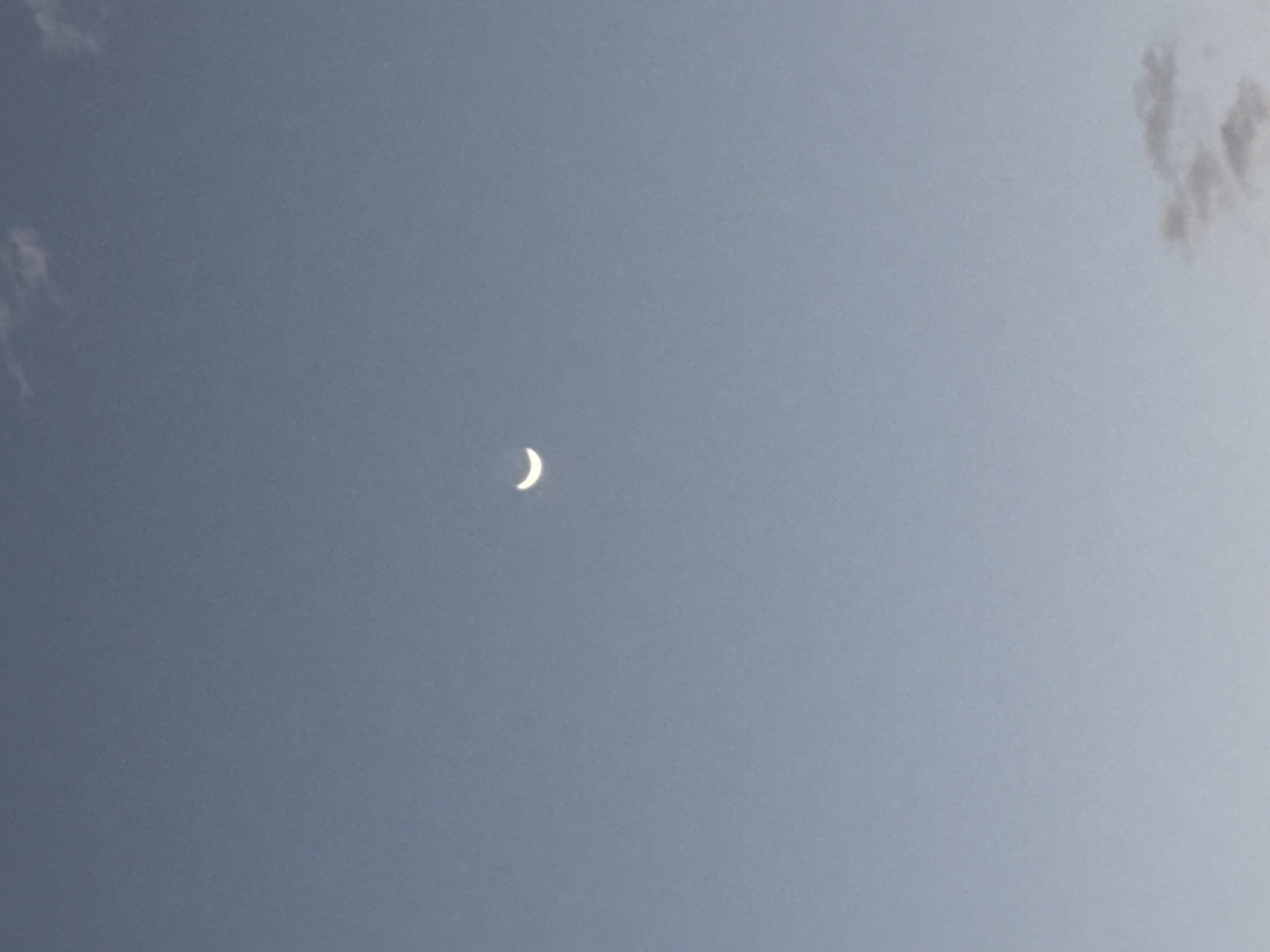A crescent moon is visible in a pale blue sky. Wisps of clouds are present in the upper and lower portions of the sky. The image does not contain any specific information to indicate a location in Corvera, Spain.