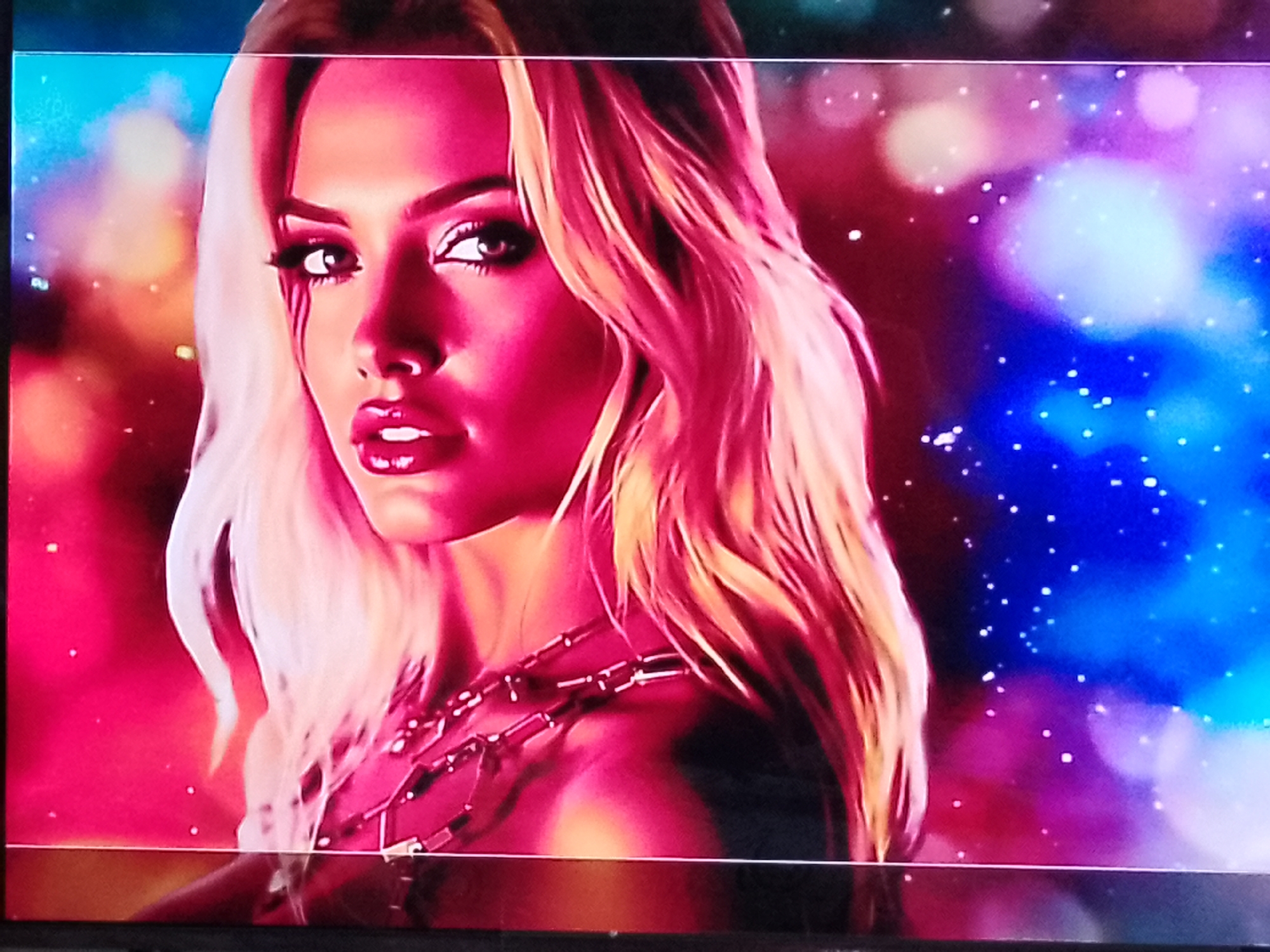 The image is a close-up shot of a woman's face and upper body. She has long, blonde, wavy hair and is wearing dark eye makeup and bright pink lipstick. She appears to be wearing a dark, possibly leather, outfit with a prominent silver necklace. The background is a colorful, blurry bokeh effect with shades of pink, blue, and purple. There are small white speckles throughout the background, resembling stars or glitter. The lighting on the woman is predominantly pink, creating a dramatic and stylized look. No specific location in Chișinău, Moldova, can be determined from the image.