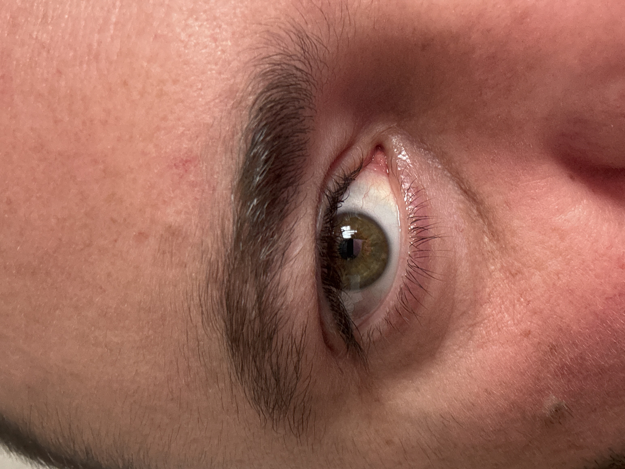 Close-up view of a human eye with dark eyelashes and eyebrow, light skin, and light-green iris. The eye is looking to the side. The photo does not include any features that can be used to identify the city or location of the subject.